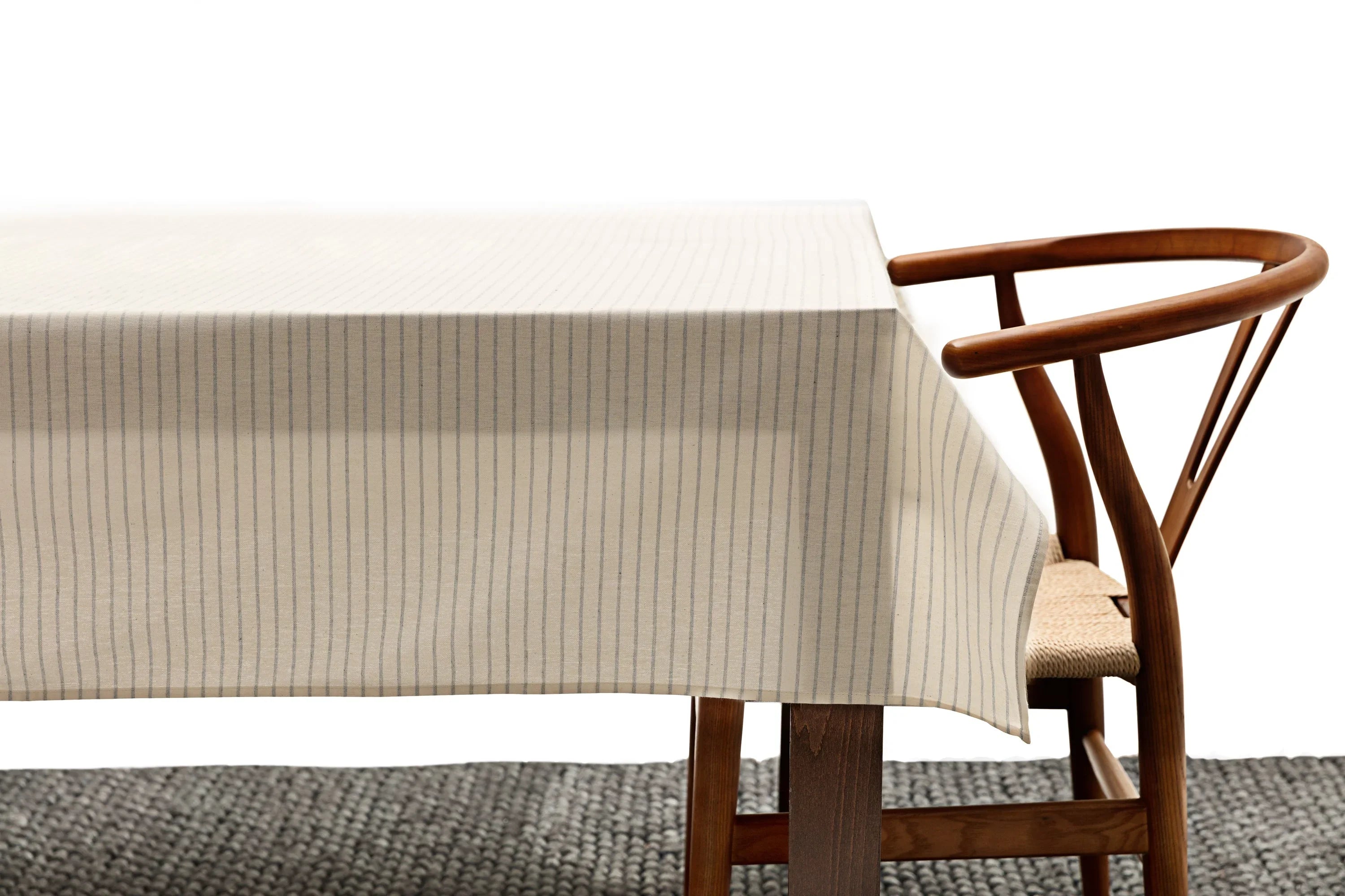 Minimalist cream tablecloth with thin blue stripes on wooden table, modern wooden chair beside it