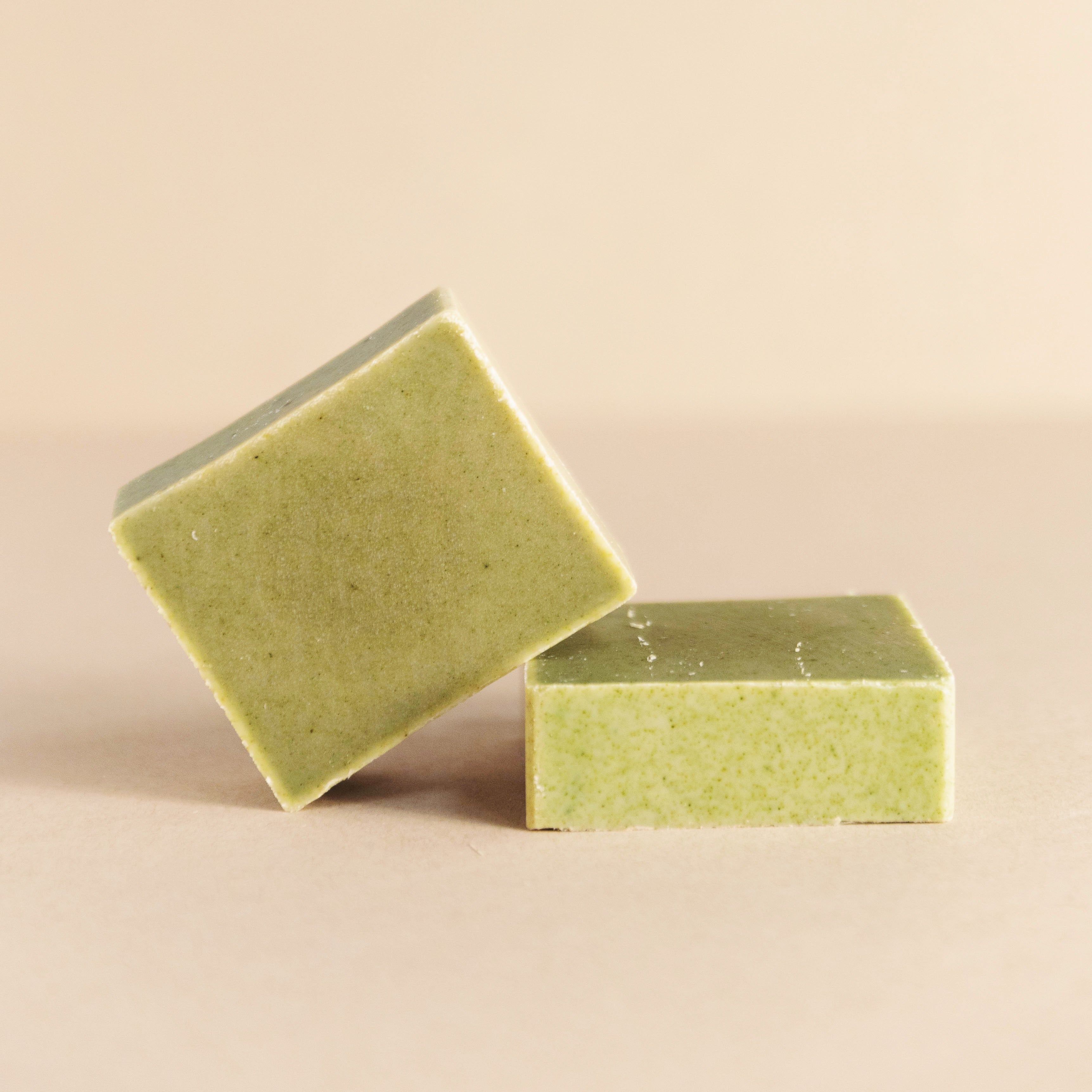 Two green square natural soap bars on a beige surface with minimal background