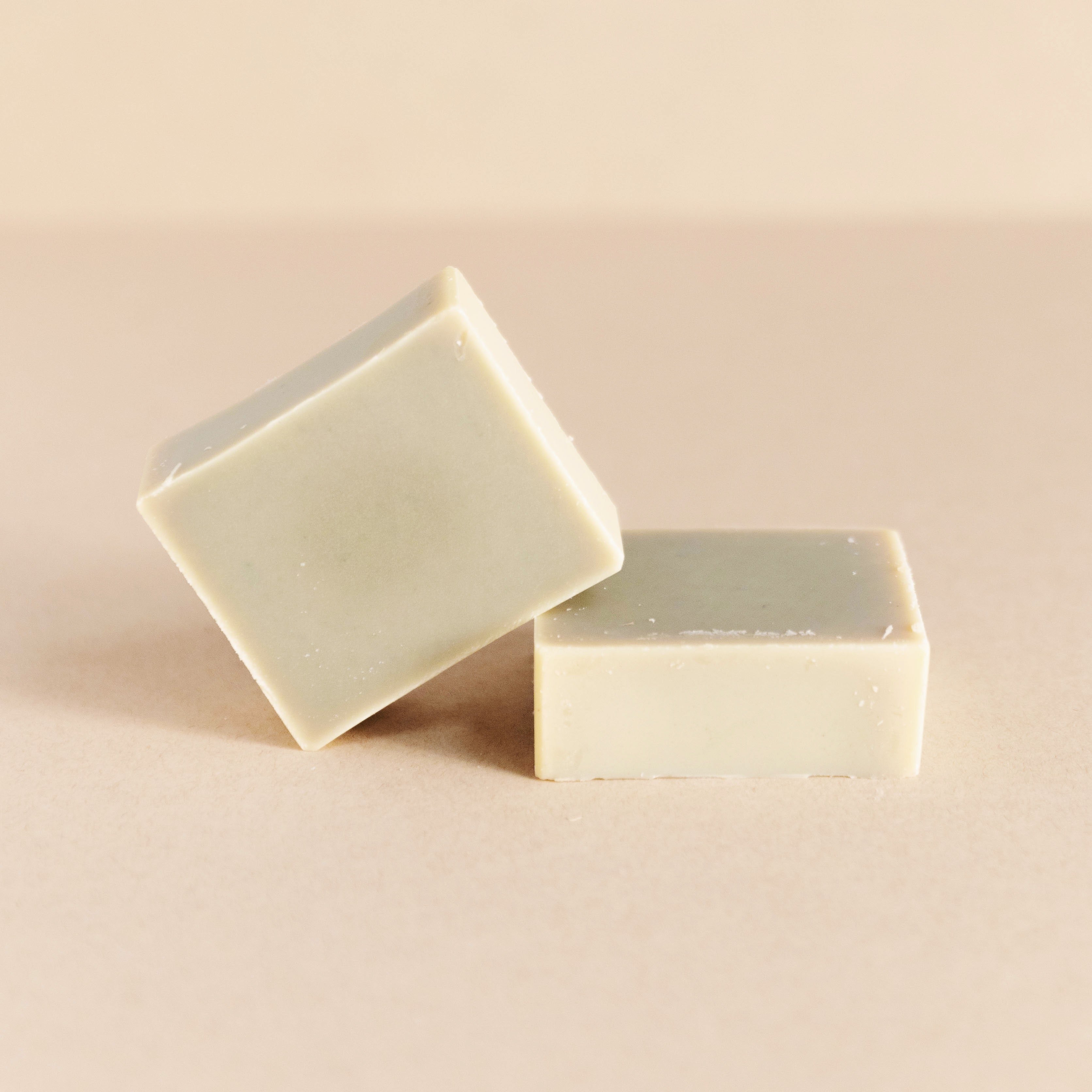 Two beige rectangular natural soap bars on a neutral beige background