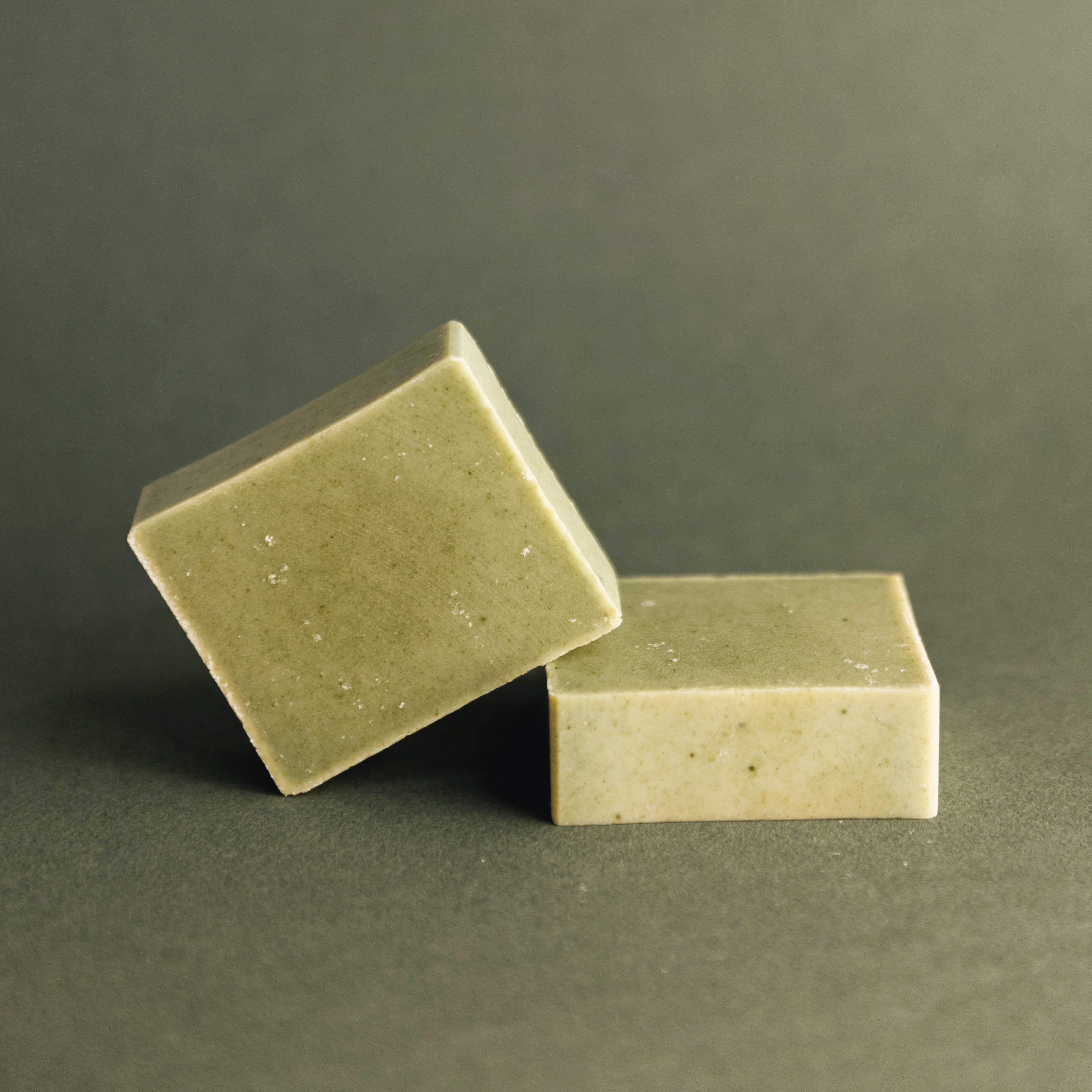 Two square green speckled natural soap bars on a matching green background