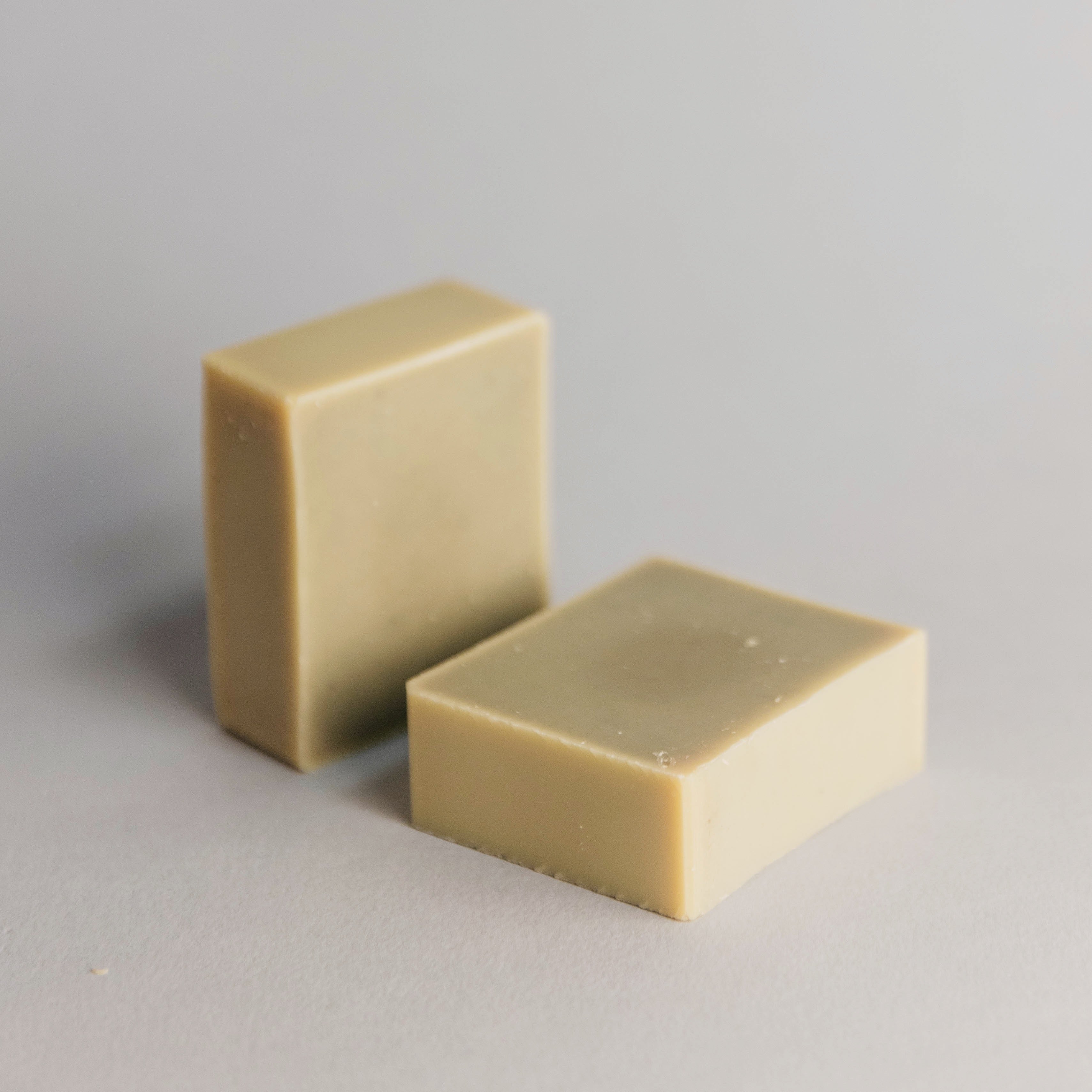 Two beige rectangular soap bars on a light gray surface with soft shadows