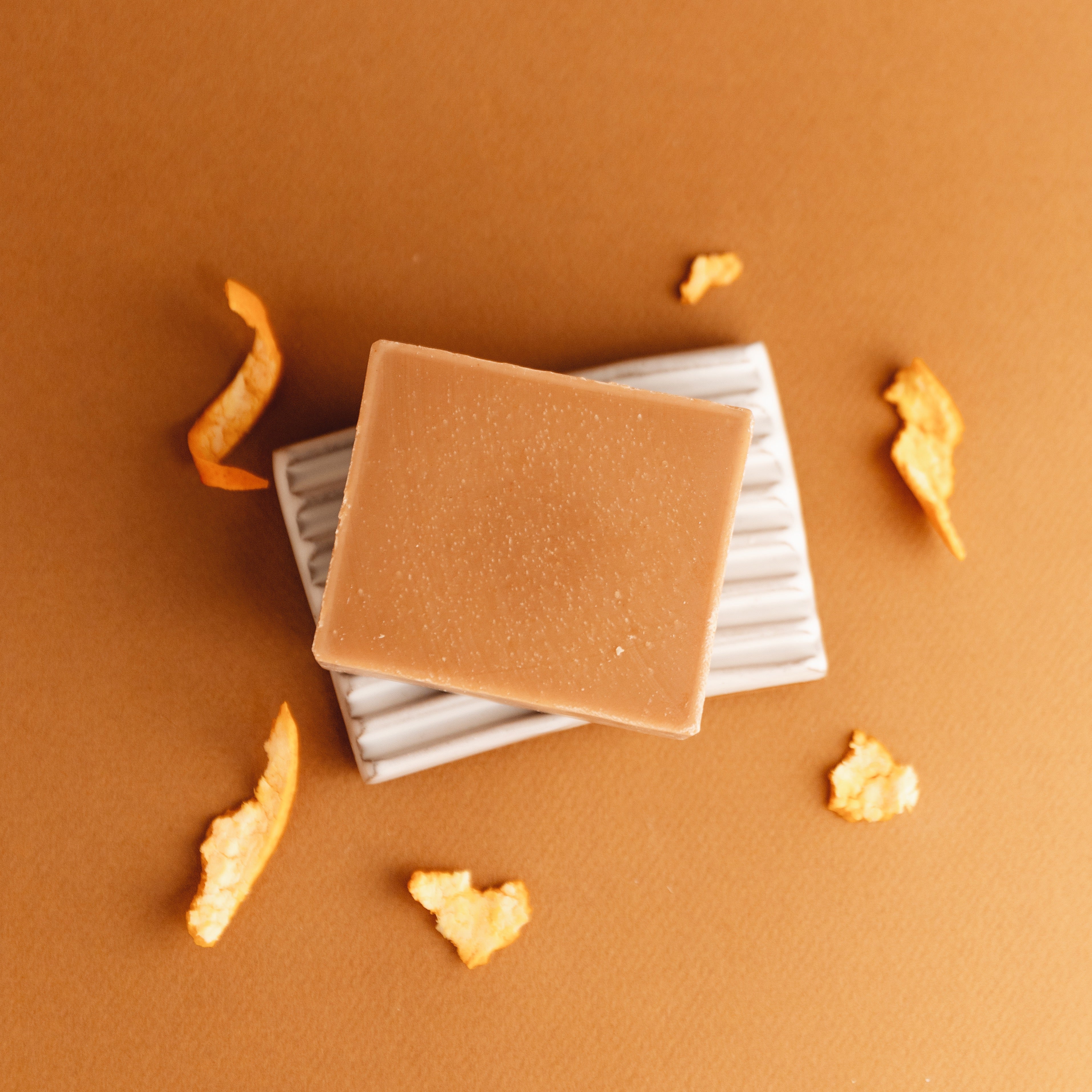 Natural brown soap bar on white dish with orange peel on brown background