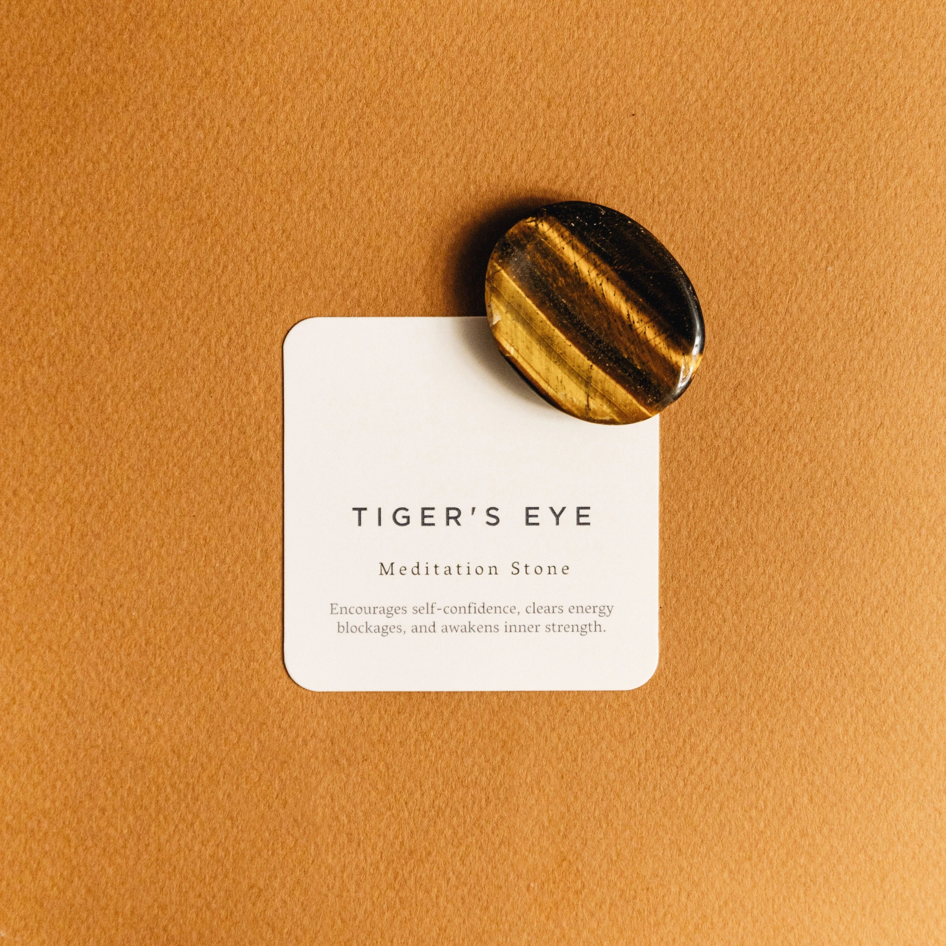 Polished tiger's eye meditation stone on card explaining its benefits on brown background