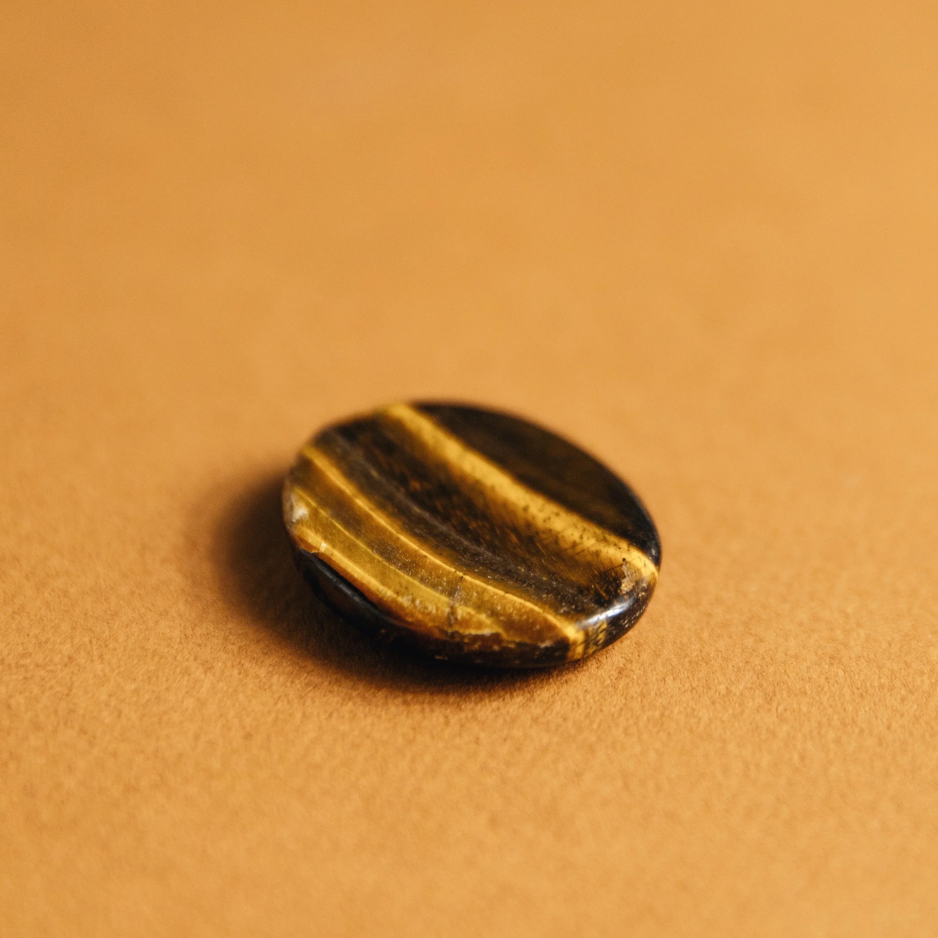 Polished tiger's eye gemstone with golden brown stripes on a warm brown background