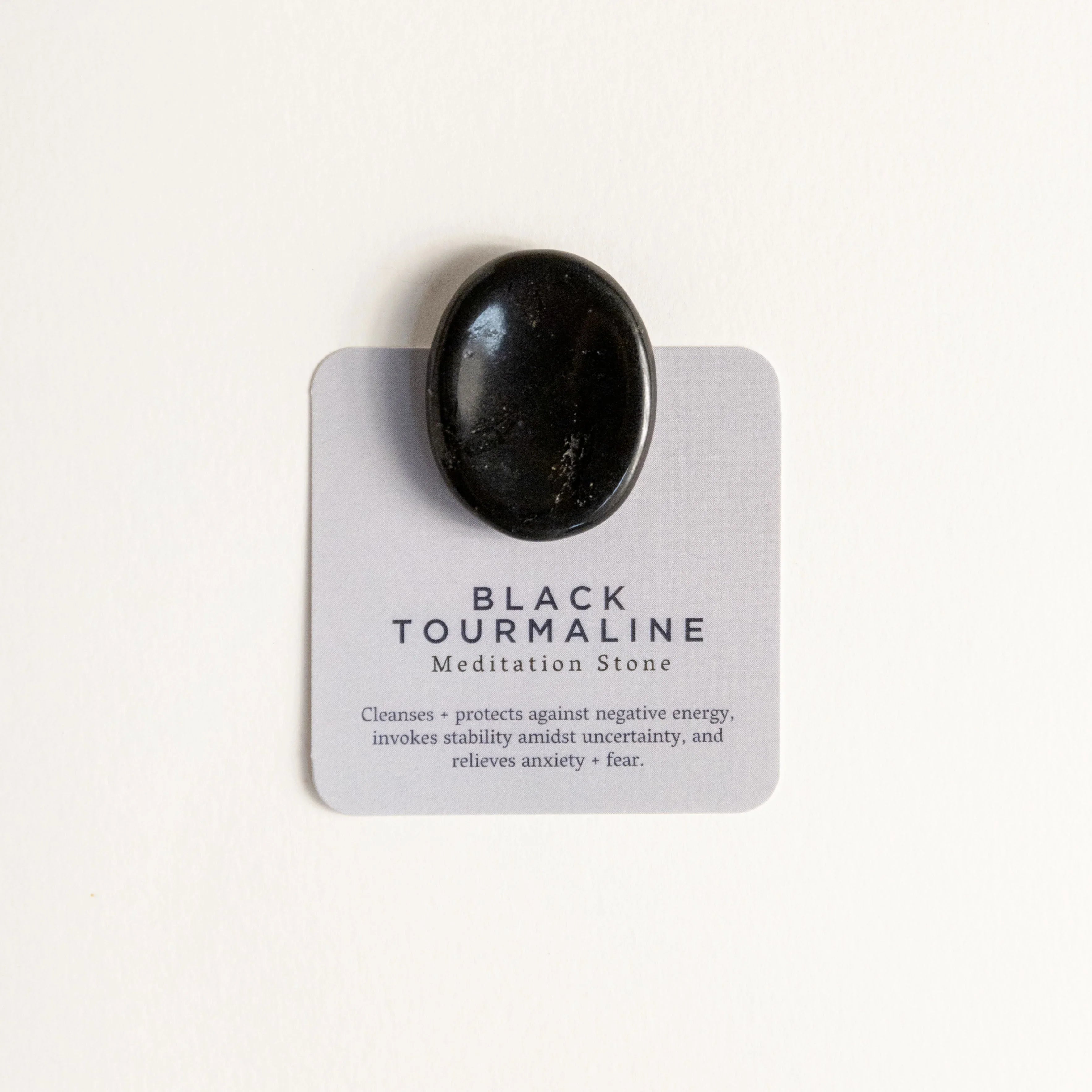 Polished black tourmaline meditation stone on information card with healing benefits text