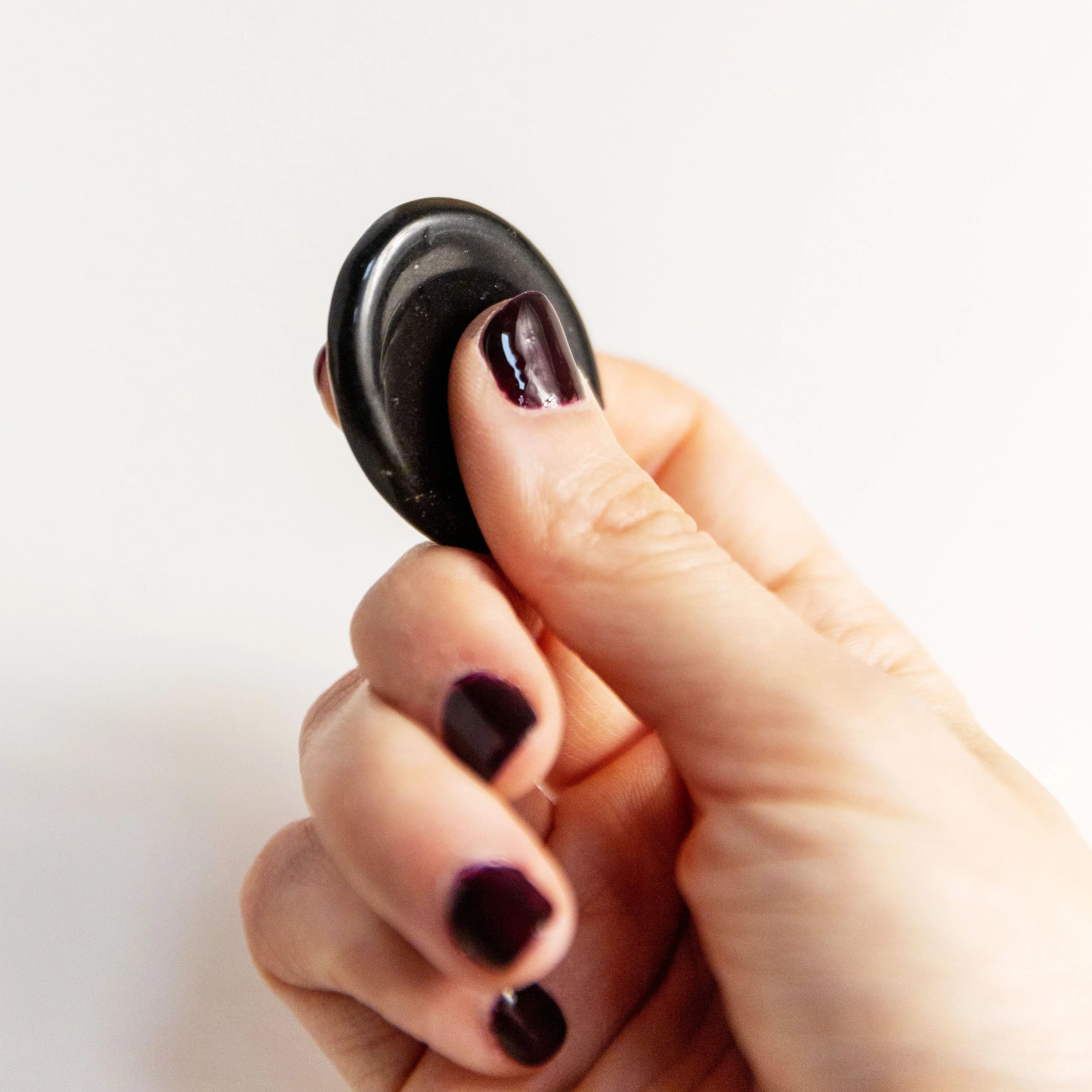 Hand with dark purple nail polish holding small smooth black massage stone