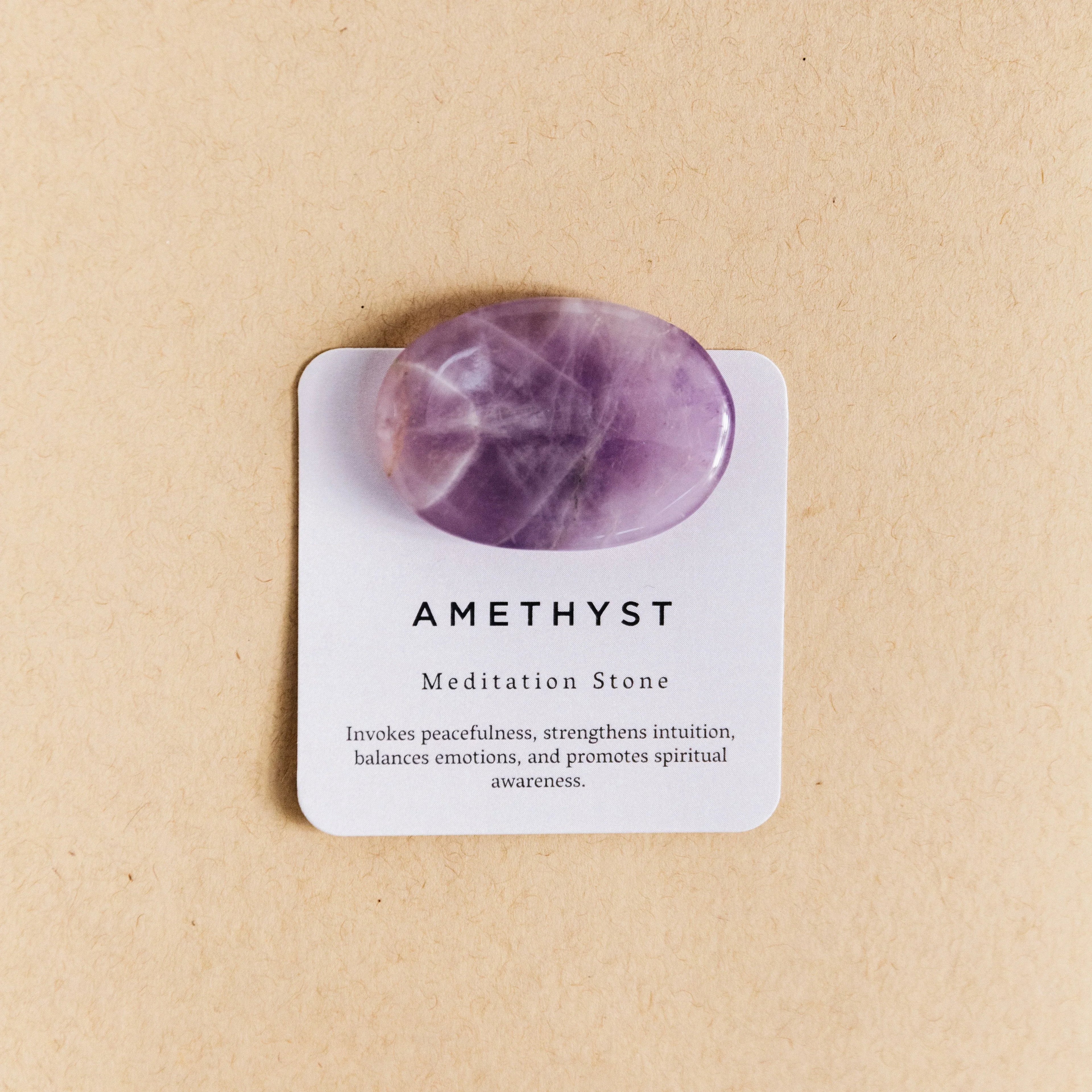 Polished purple amethyst meditation stone on a beige card with spiritual benefits text