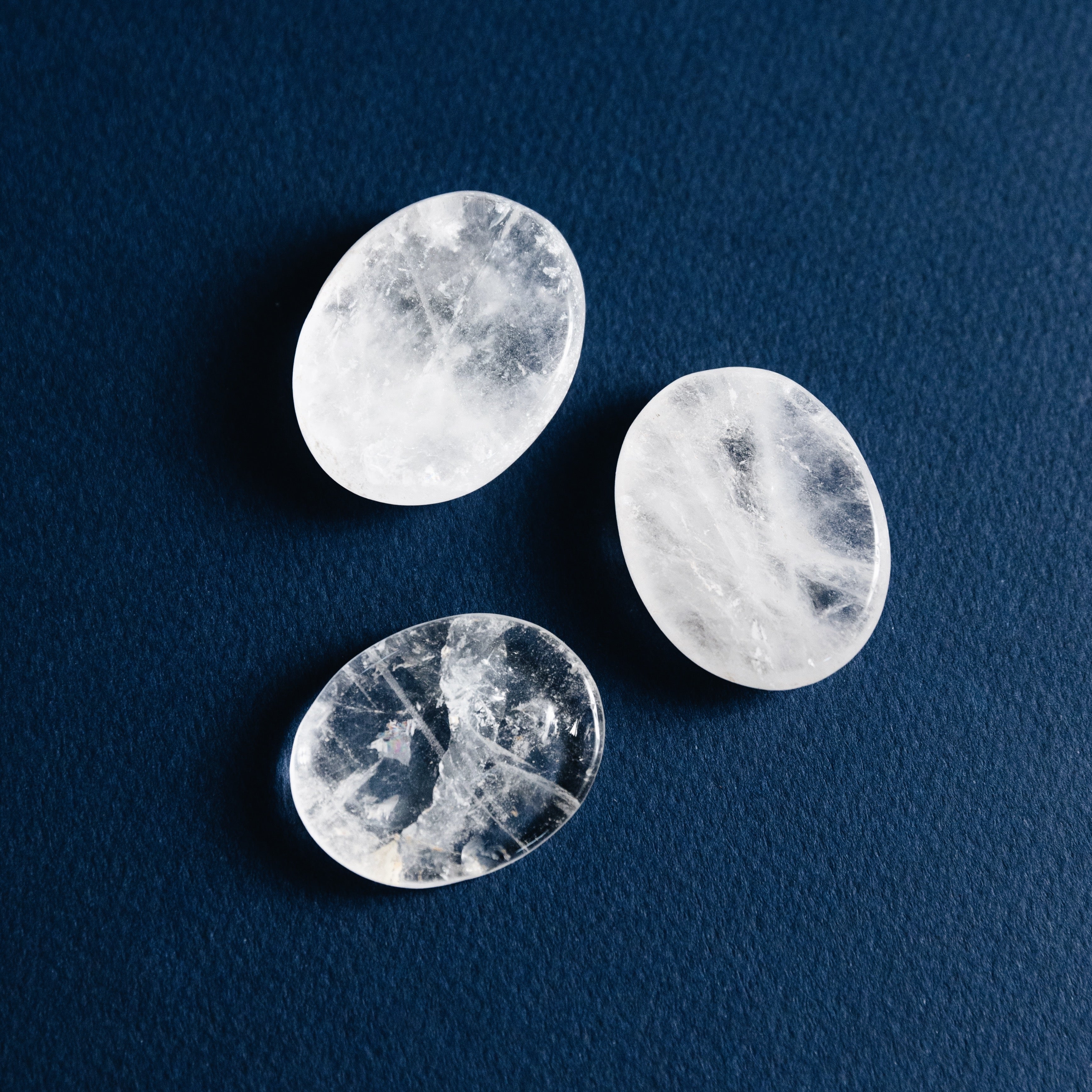 Three polished clear quartz stones with natural inclusions on a dark blue textured surface