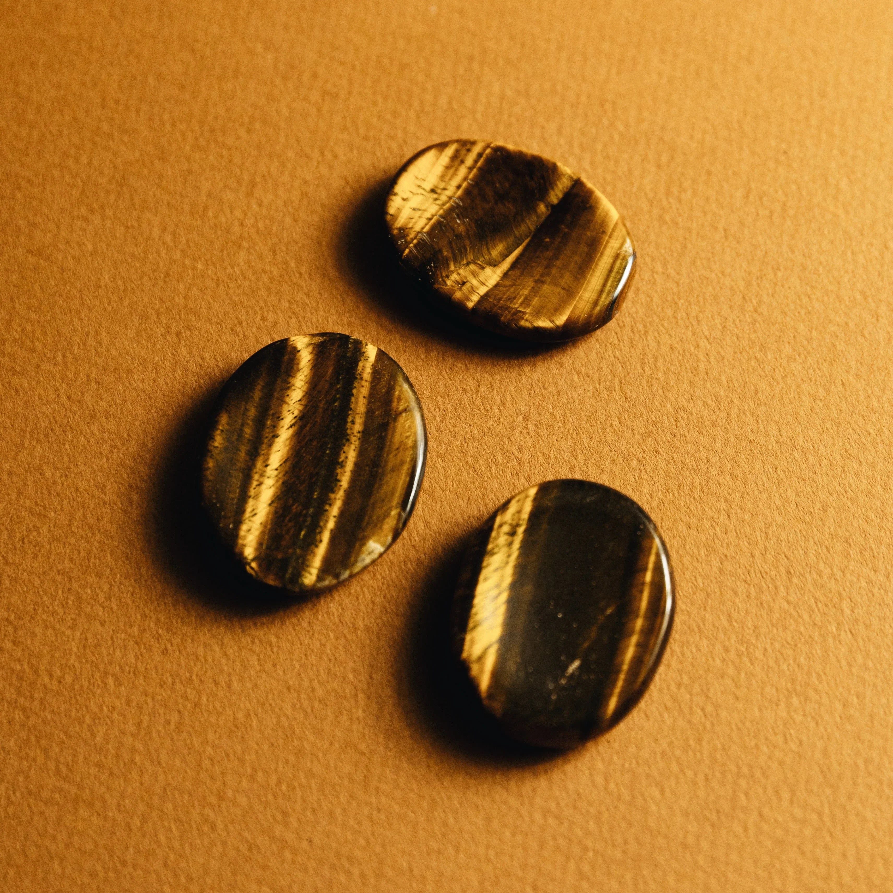 Three polished tiger's eye stones on a textured brown surface