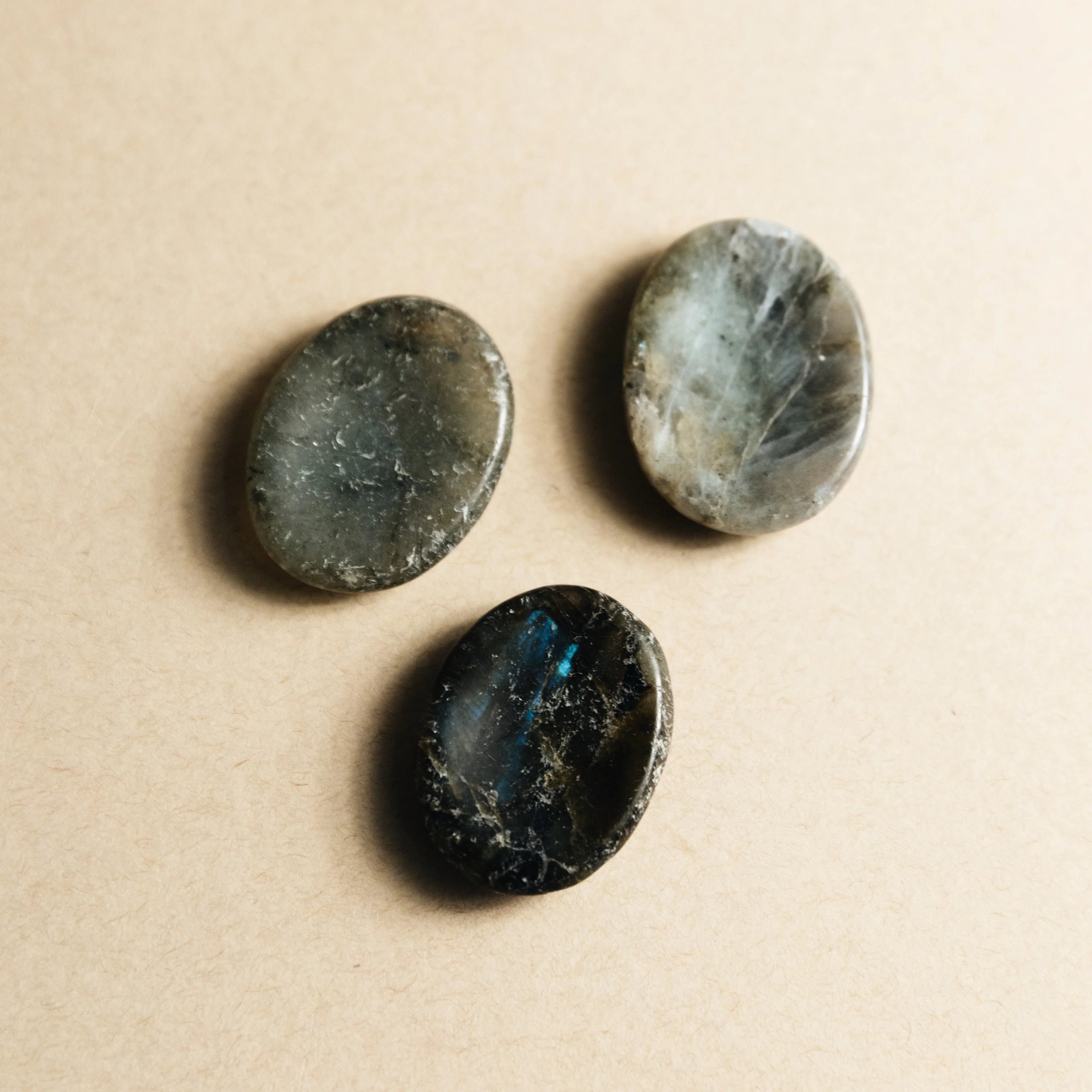 Three polished labradorite stones with gray and blue iridescence on beige background