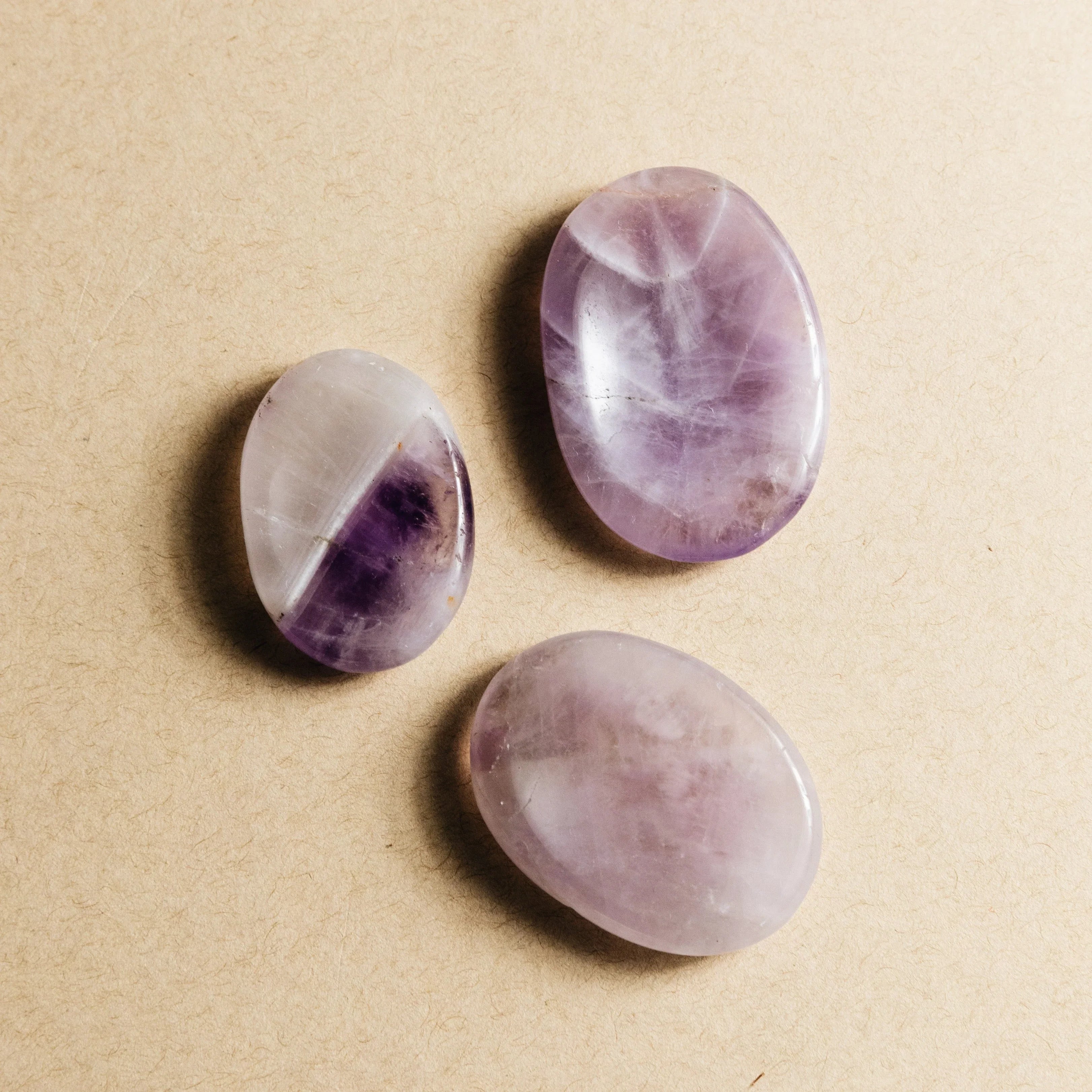 Three polished amethyst stones with purple hues on a beige textured surface