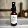 Amber glass bottle of Slow North Linen Spray Embers + Leather on marble surface with blurred background