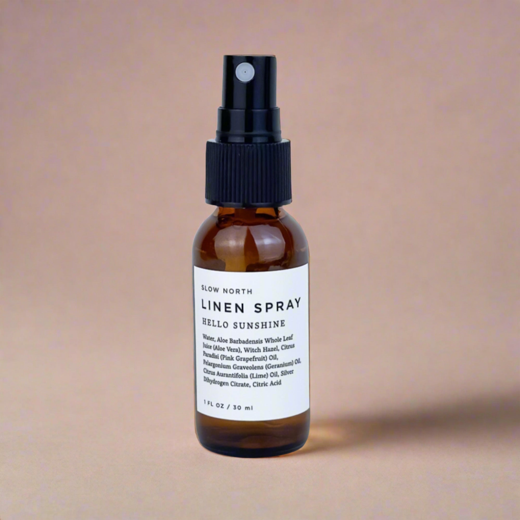 Amber glass bottle of Slow North Hello Sunshine linen spray with black spray top on beige background