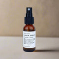 Brown glass bottle of Slow North Orange + Clove linen spray with black spray top on beige background