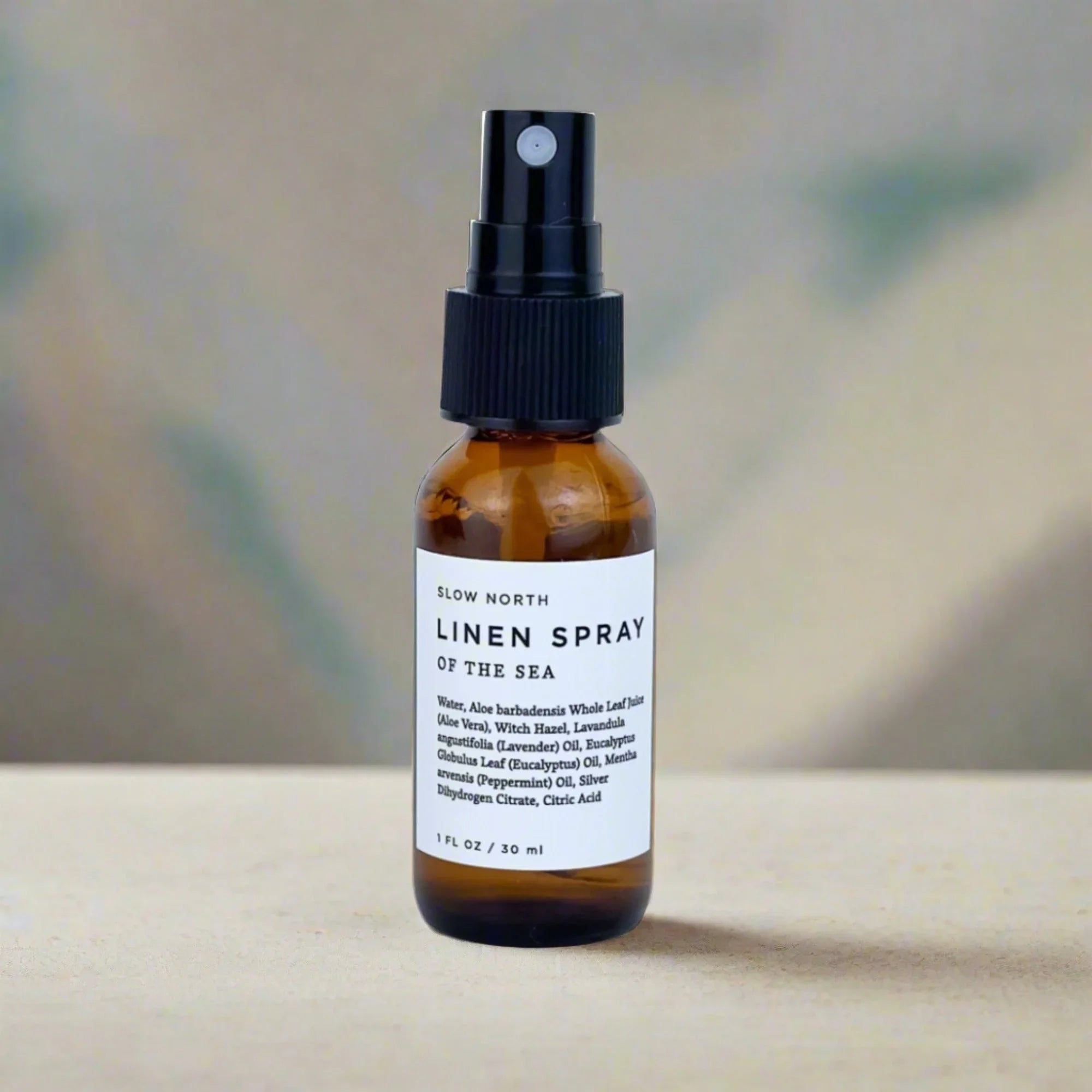 Slow North Linen Spray Of The Sea in 1 fl oz brown glass spray bottle on beige surface