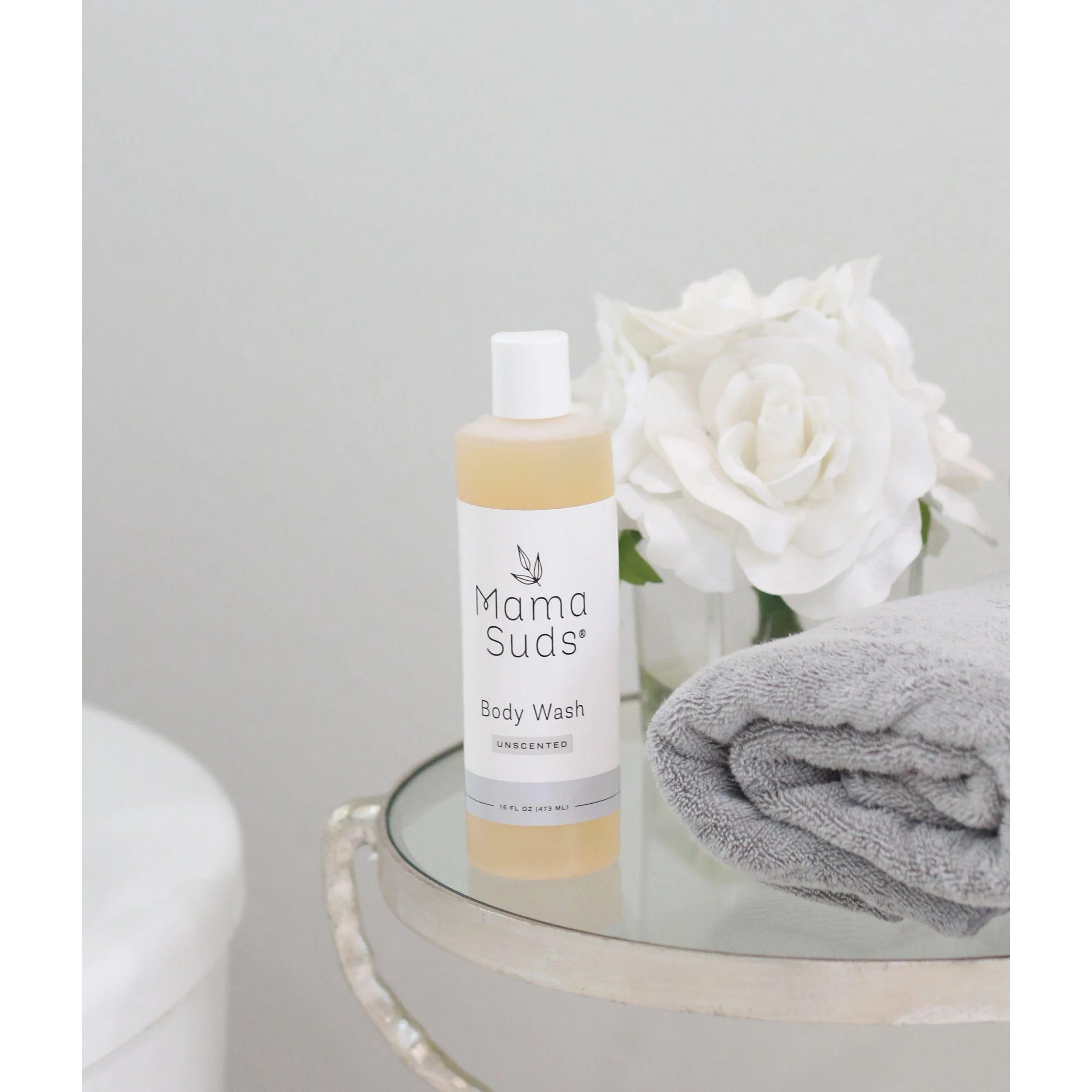 Mama Suds body wash bottle on glass table with white roses and gray towel, Qu!rk Boutique