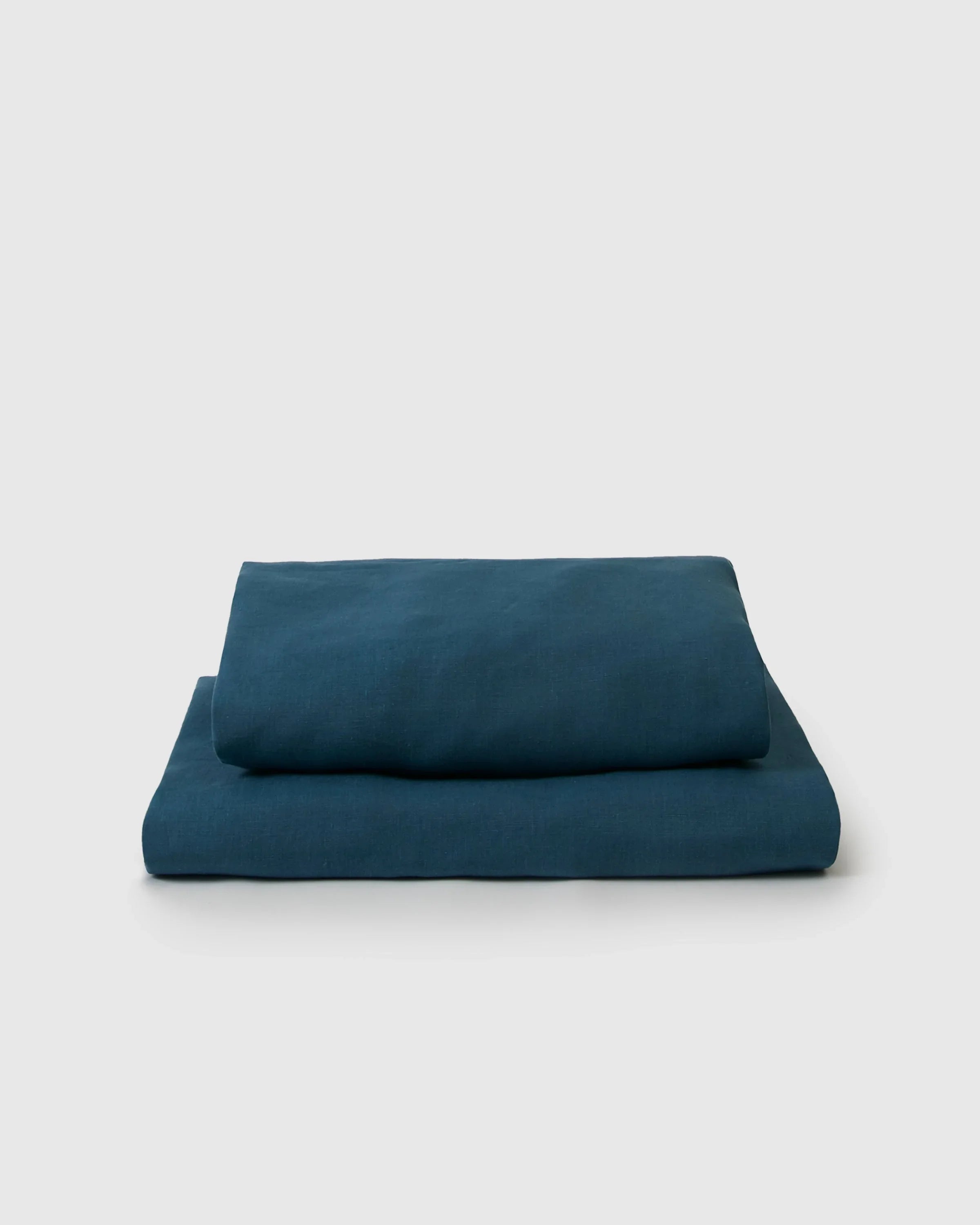Folded dark teal linen flat and fitted sheet set on a plain background, Qu!rk Boutique