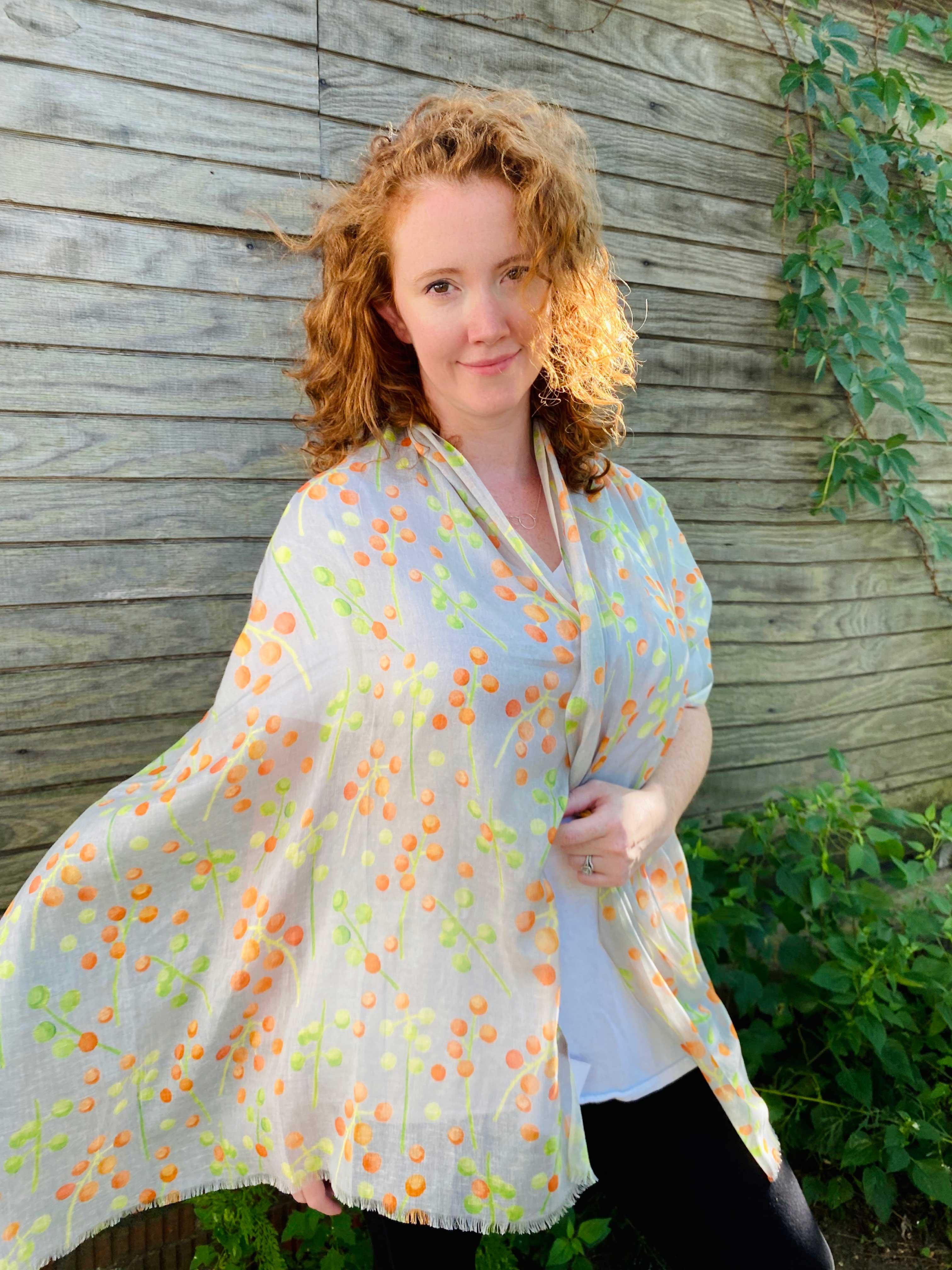 Woman with curly hair wearing a light scarf with orange and green berry pattern outdoors