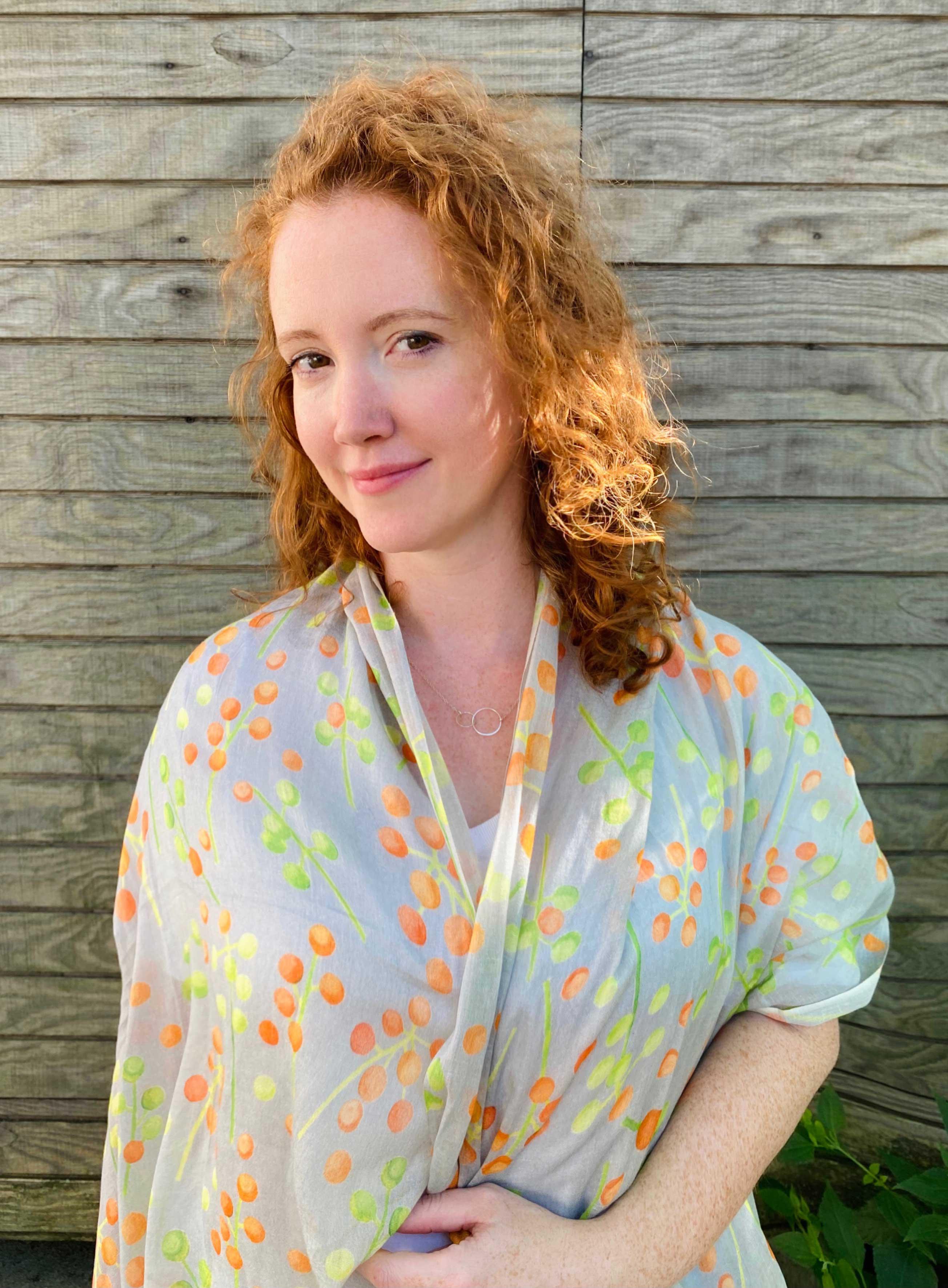 Red-haired woman wearing a floral orange and green patterned scarf against a wooden background