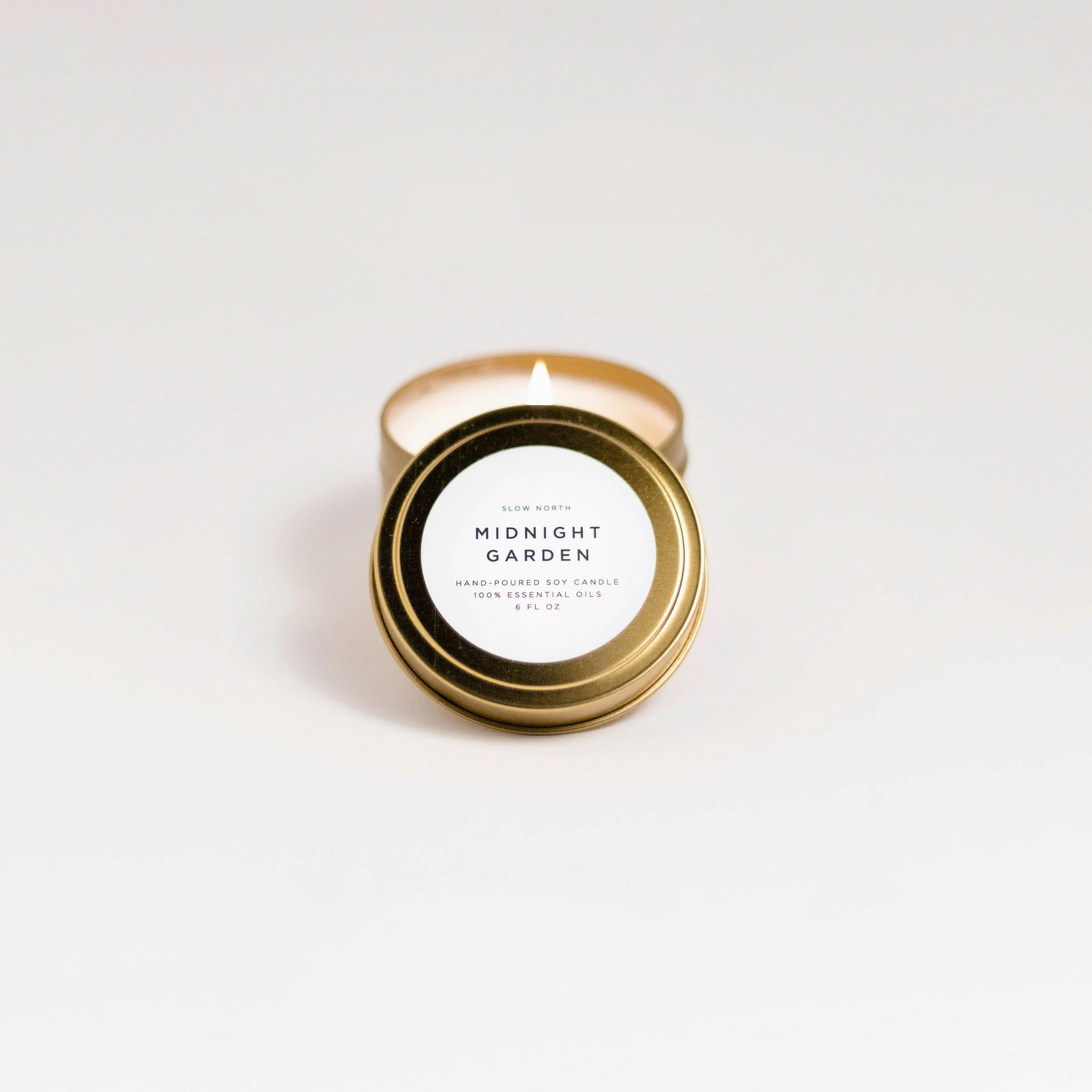 Lit Midnight Garden travel tin soy candle with gold lid and white label on white background