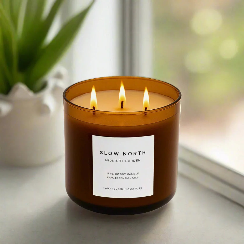Slow North Midnight Garden 3-wick soy candle burning in amber glass jar on marble surface