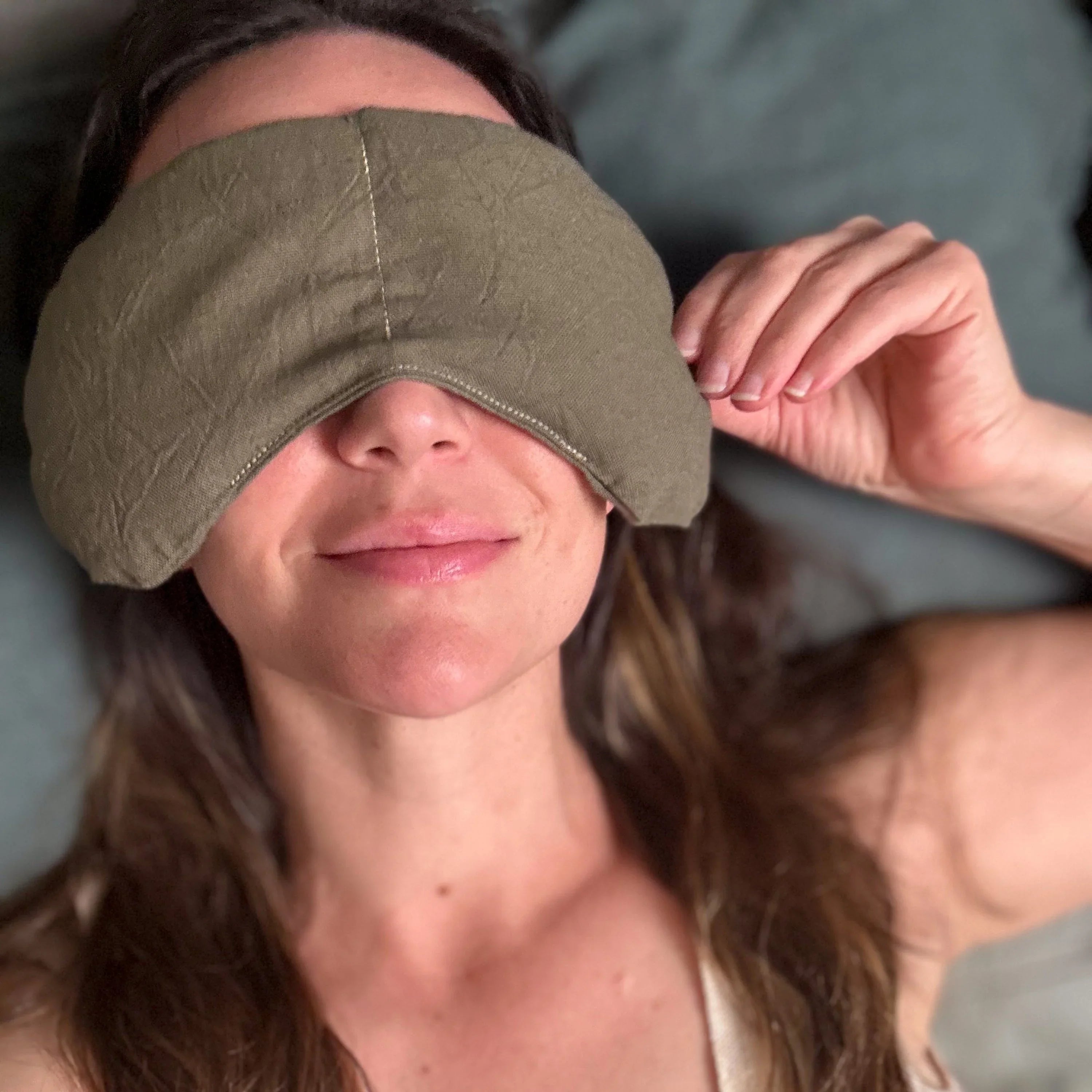 Woman lying down wearing olive green migraine relief eye mask covering eyes