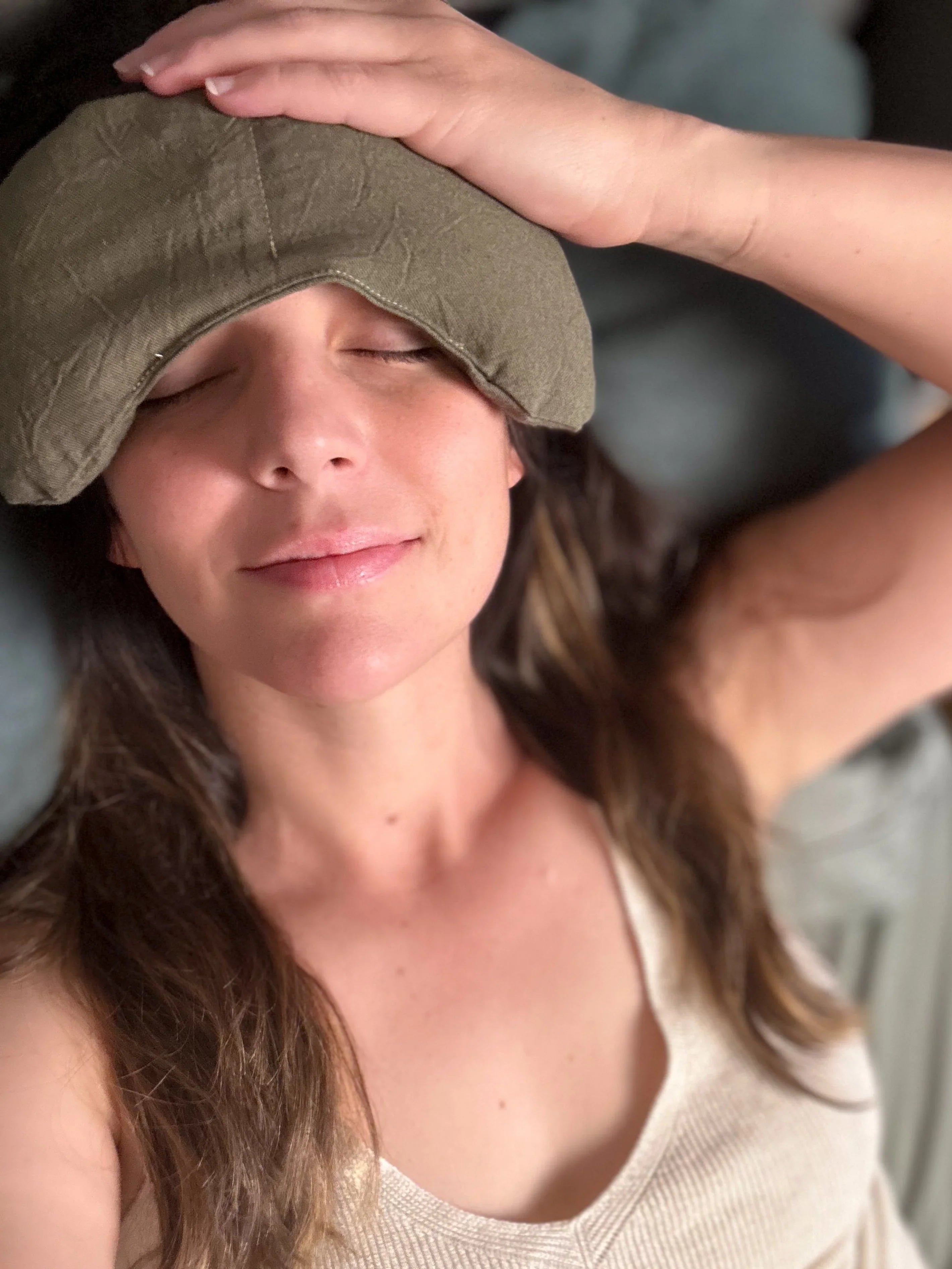 Woman lying down with eyes closed wearing olive green migraine relief mask for headache pain