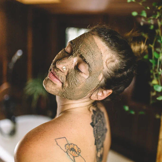 Woman with clay face mask, floral tattoos, in a serene spa setting at Qu!rk Boutique