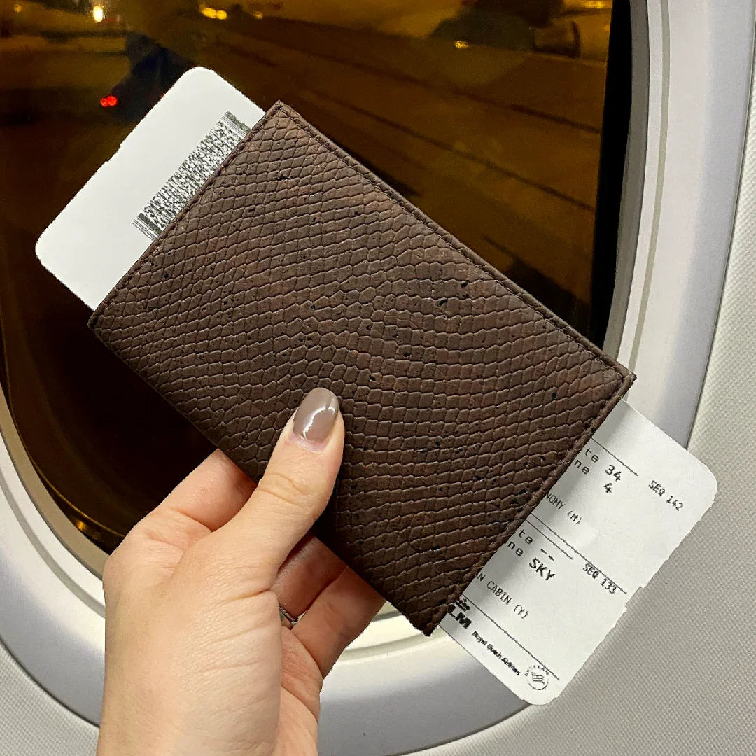 Hand holding textured brown wallet with boarding pass by airplane window, Qu!rk Boutique style