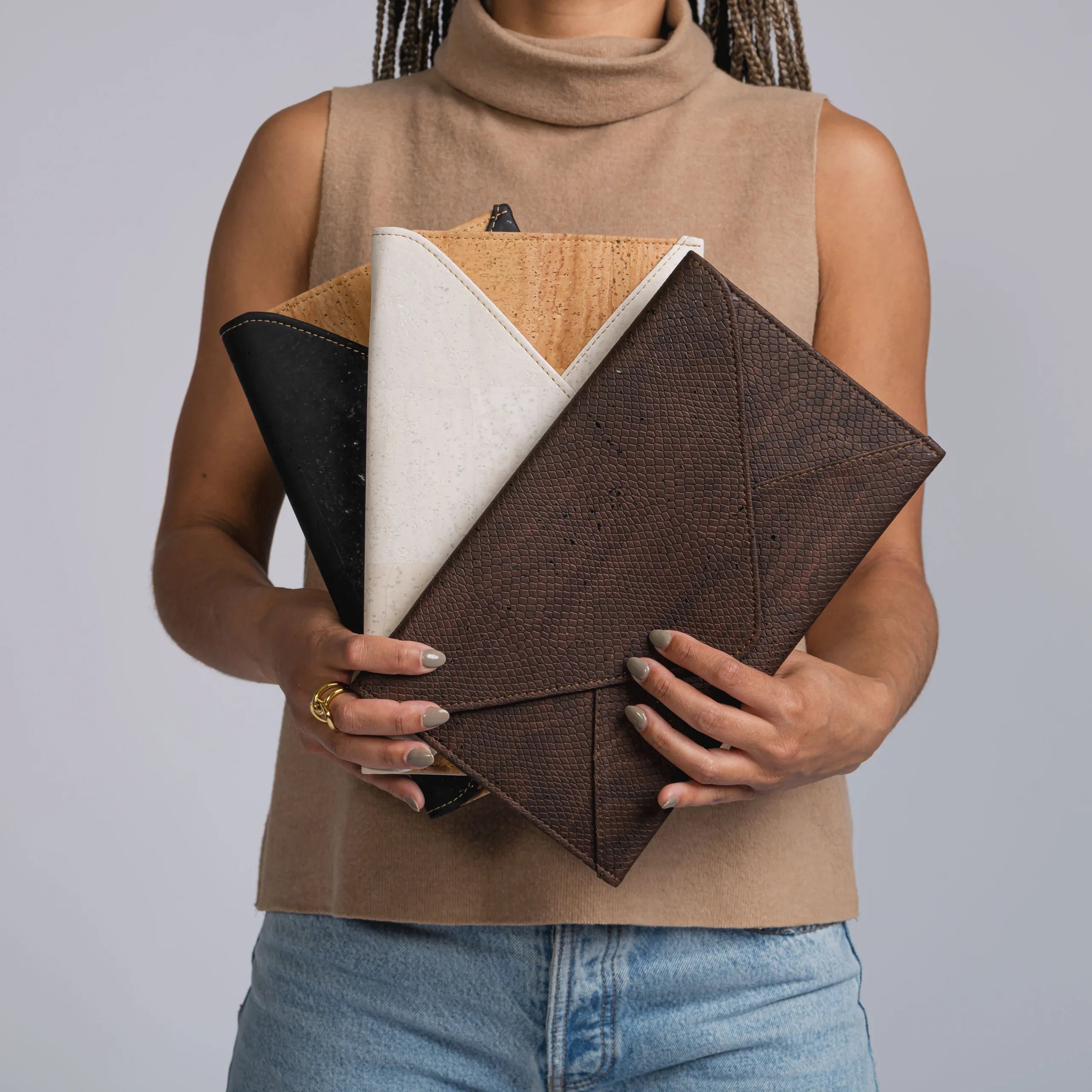 Woman holding three eco-friendly cork clutches in black, white, and brown at Qu!rk Boutique