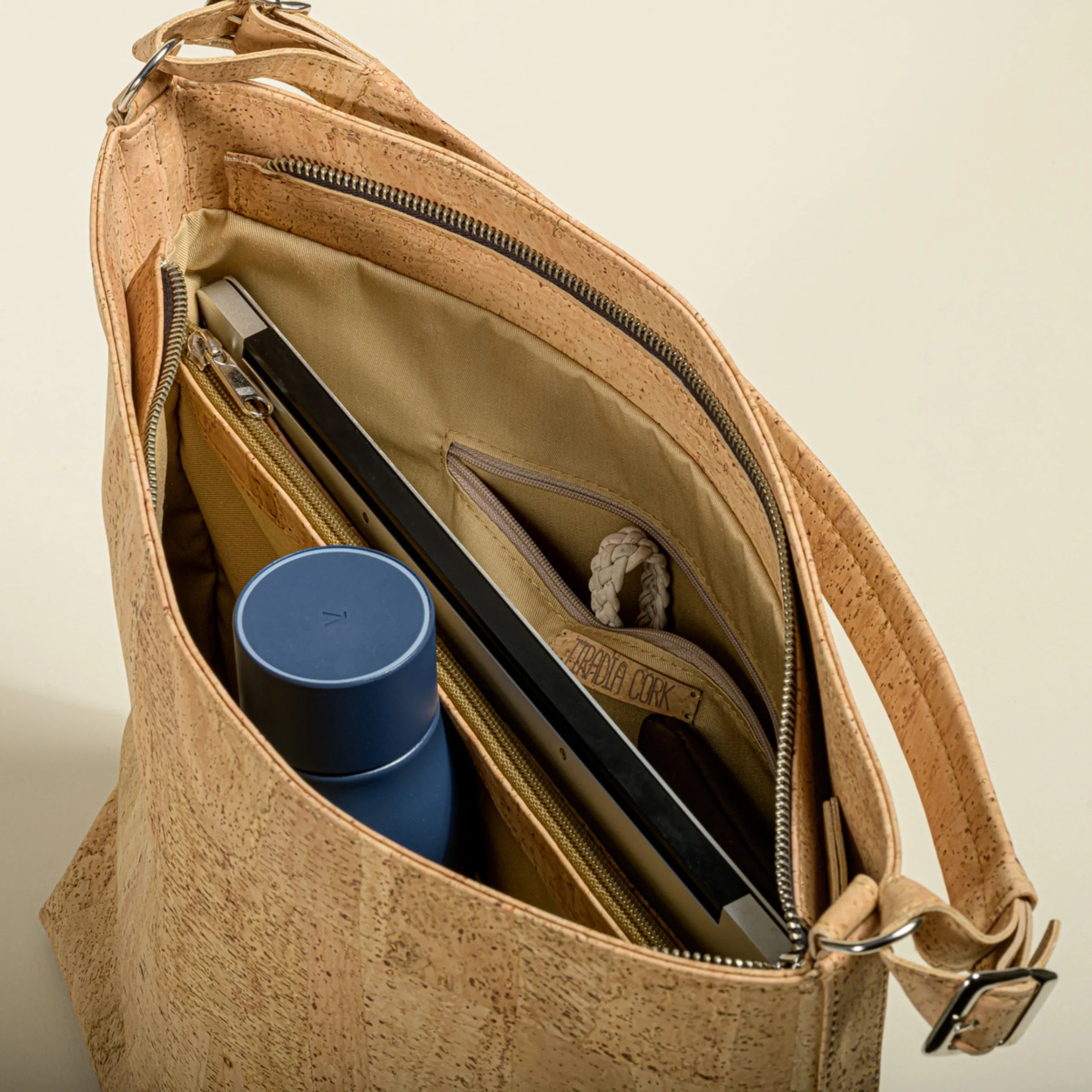 Top view of a cork handbag with organized pockets holding a blue reusable bottle and tablet