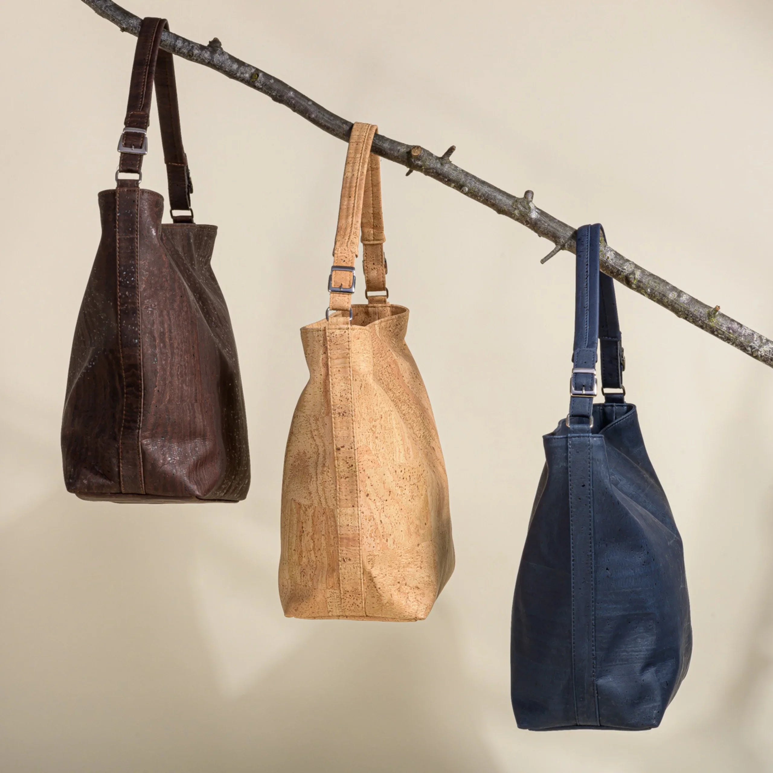 Three sustainable cork tote bags in brown, beige, and navy hanging from a branch, Qu!rk Boutique