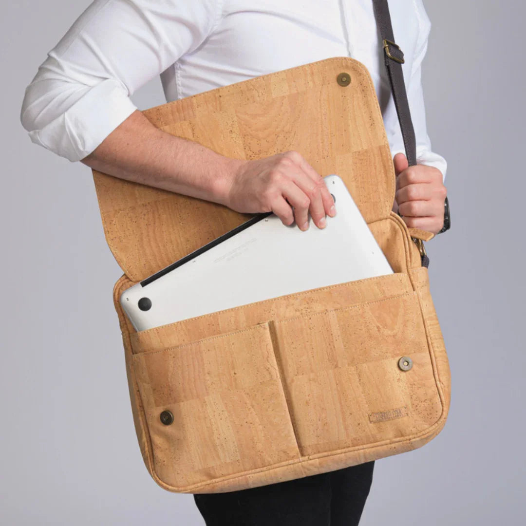 Person placing a laptop into a tan cork messenger bag from Qu!rk Boutique, eco-friendly gift