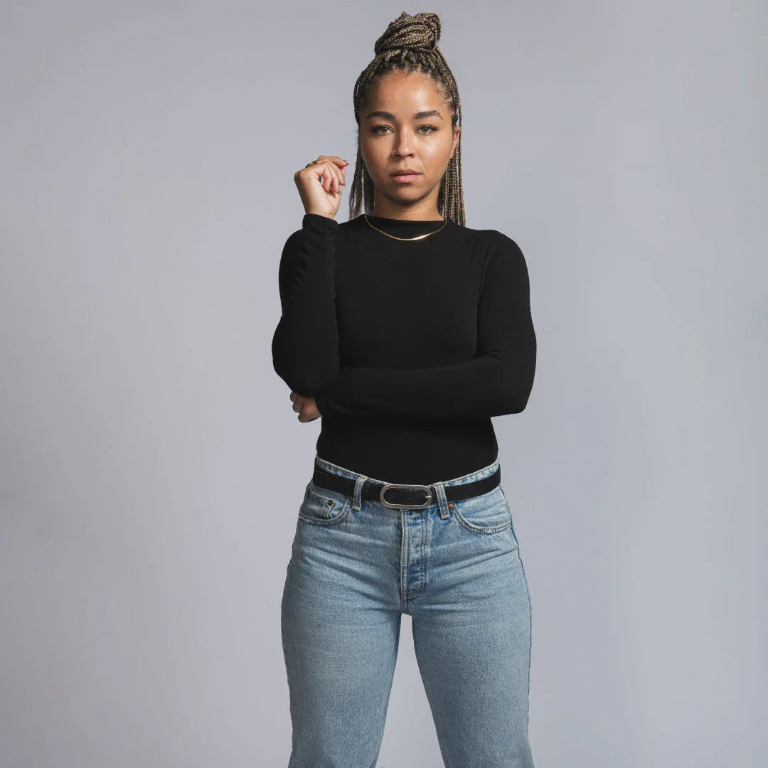 Woman in black long-sleeve top and jeans poses confidently, showcasing boutique fashion