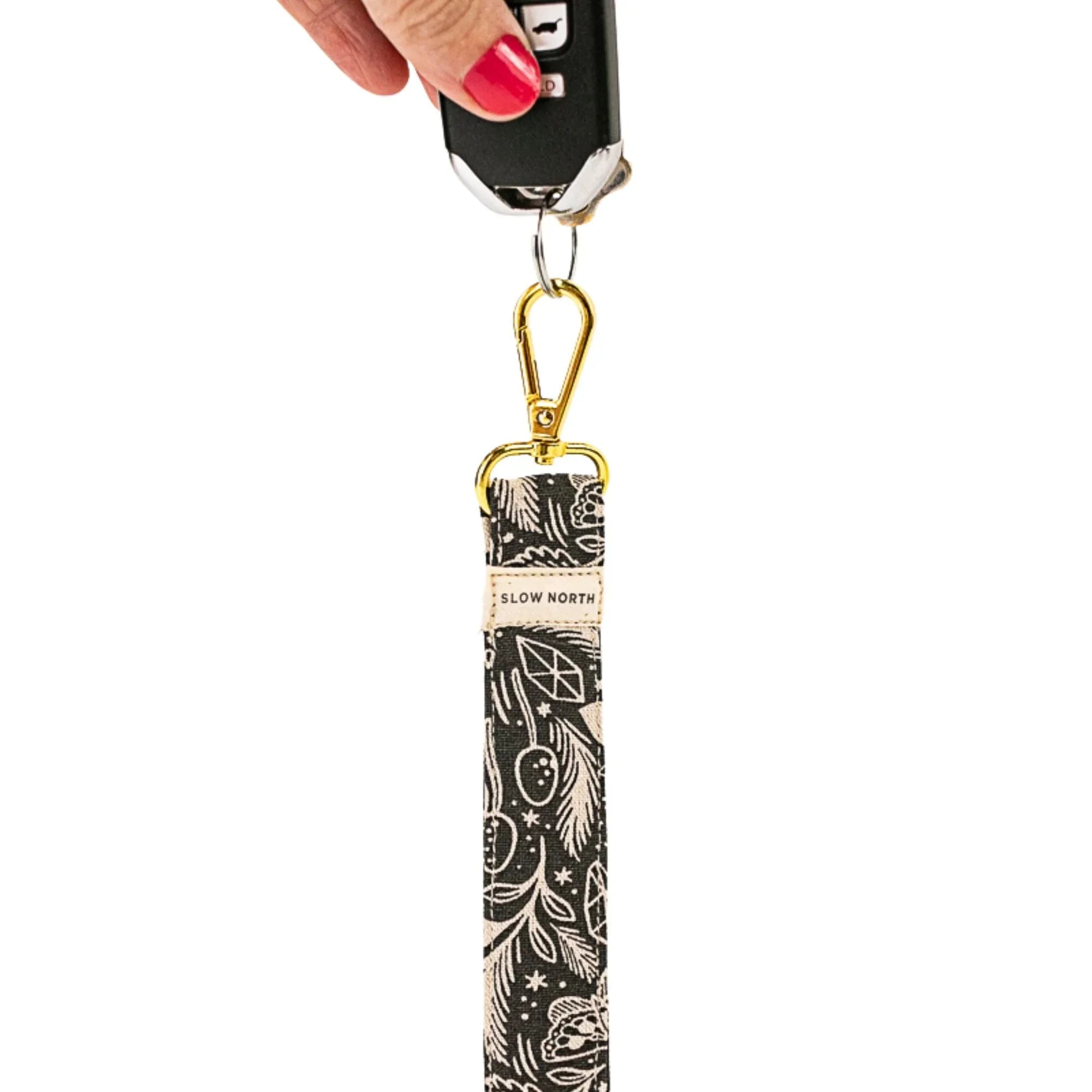 Hand holding black car key attached to Slow North fabric wristlet keychain with white botanical print and gold clasp