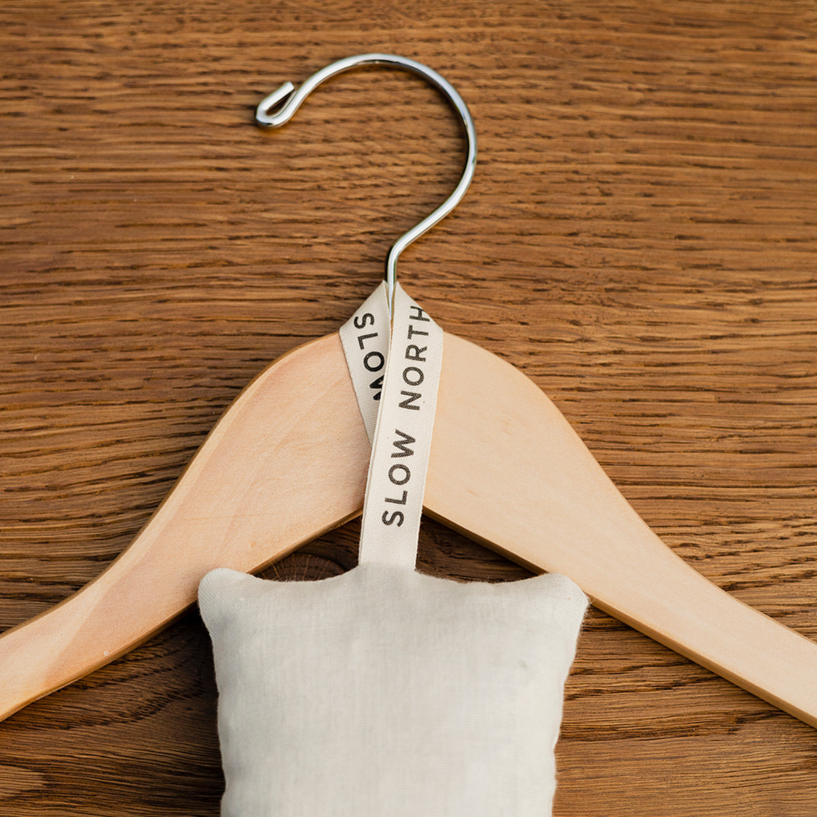 Natural cedar sachet with Slow North branded loop hanging on wooden clothes hanger