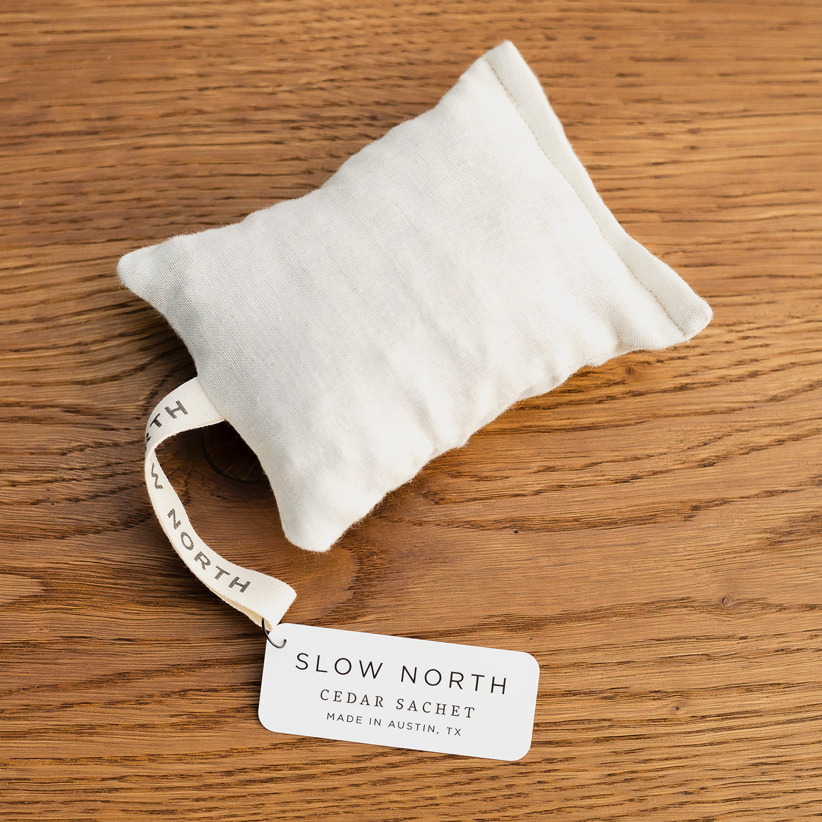 Slow North cedar sachet with white fabric and label on wooden surface
