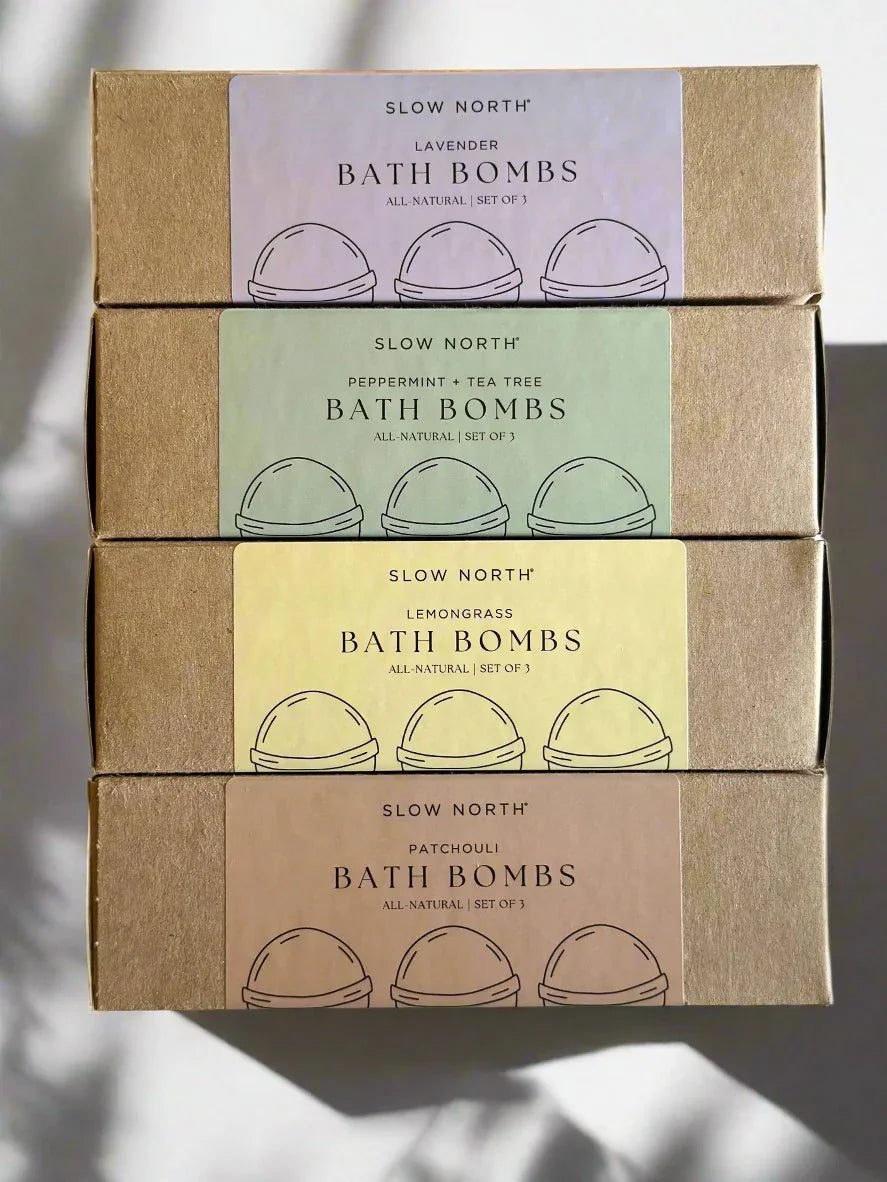 Four stacked Slow North all-natural bath bombs boxes in lavender, peppermint+tea tree, lemongrass, and patchouli scents