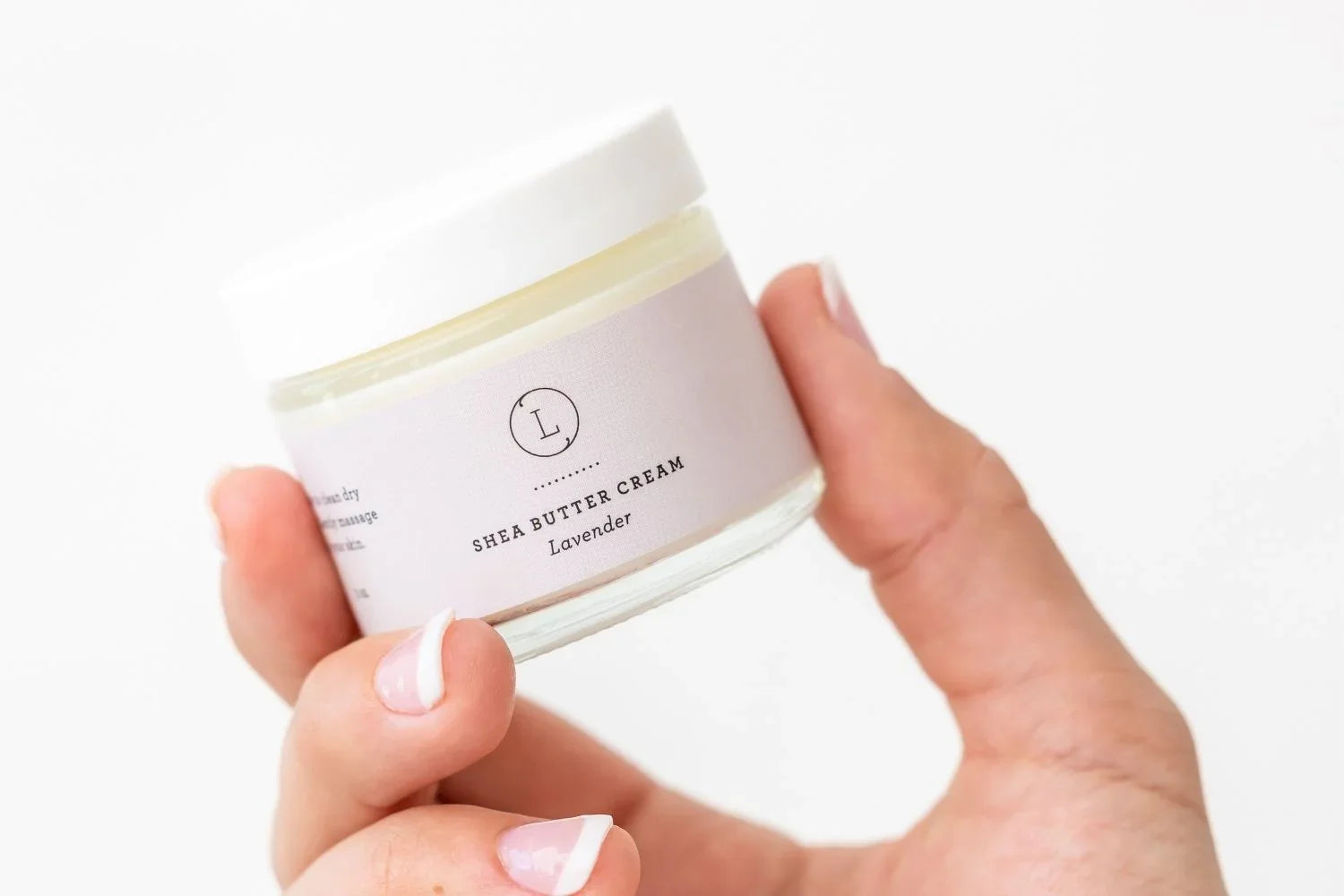 Hand holding a jar of lavender shea butter cream with white lid and label