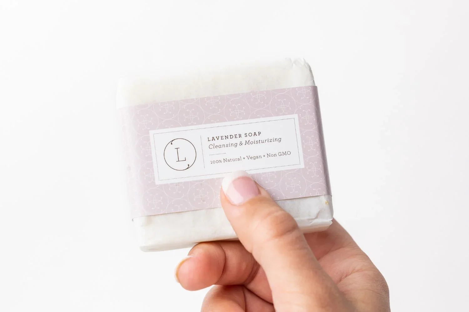Hand holding natural lavender soap bar with vegan, non-GMO label on light purple packaging