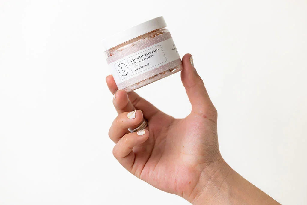 Hand holding jar of natural lavender bath salts labeled calming and relaxing