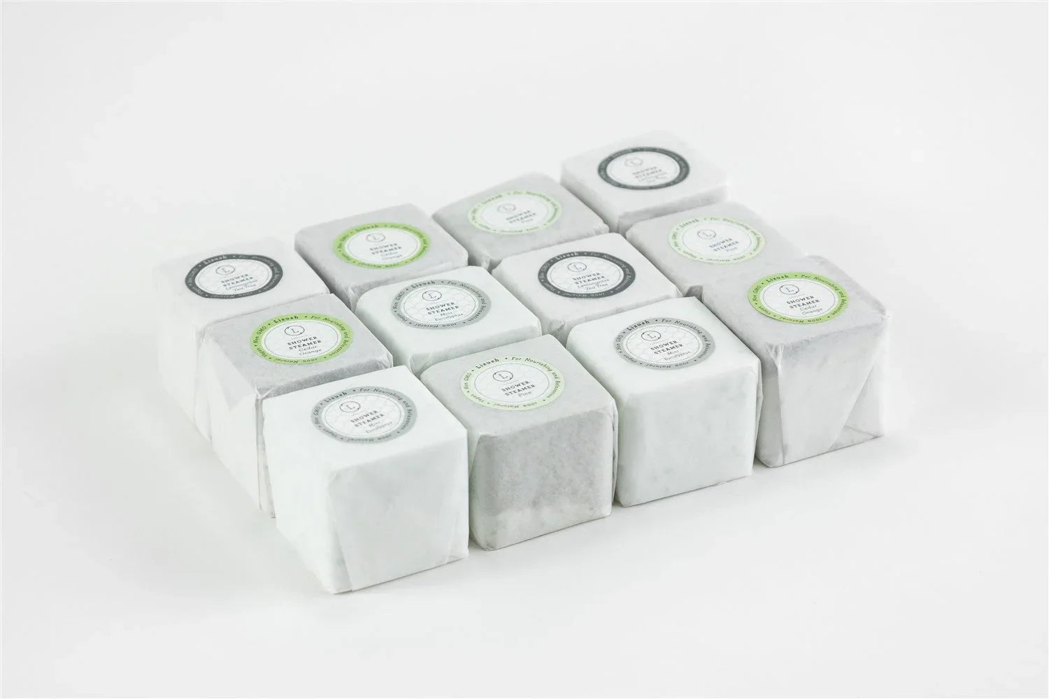 Twelve natural shower steamers wrapped in white paper, arranged in rows on a white background