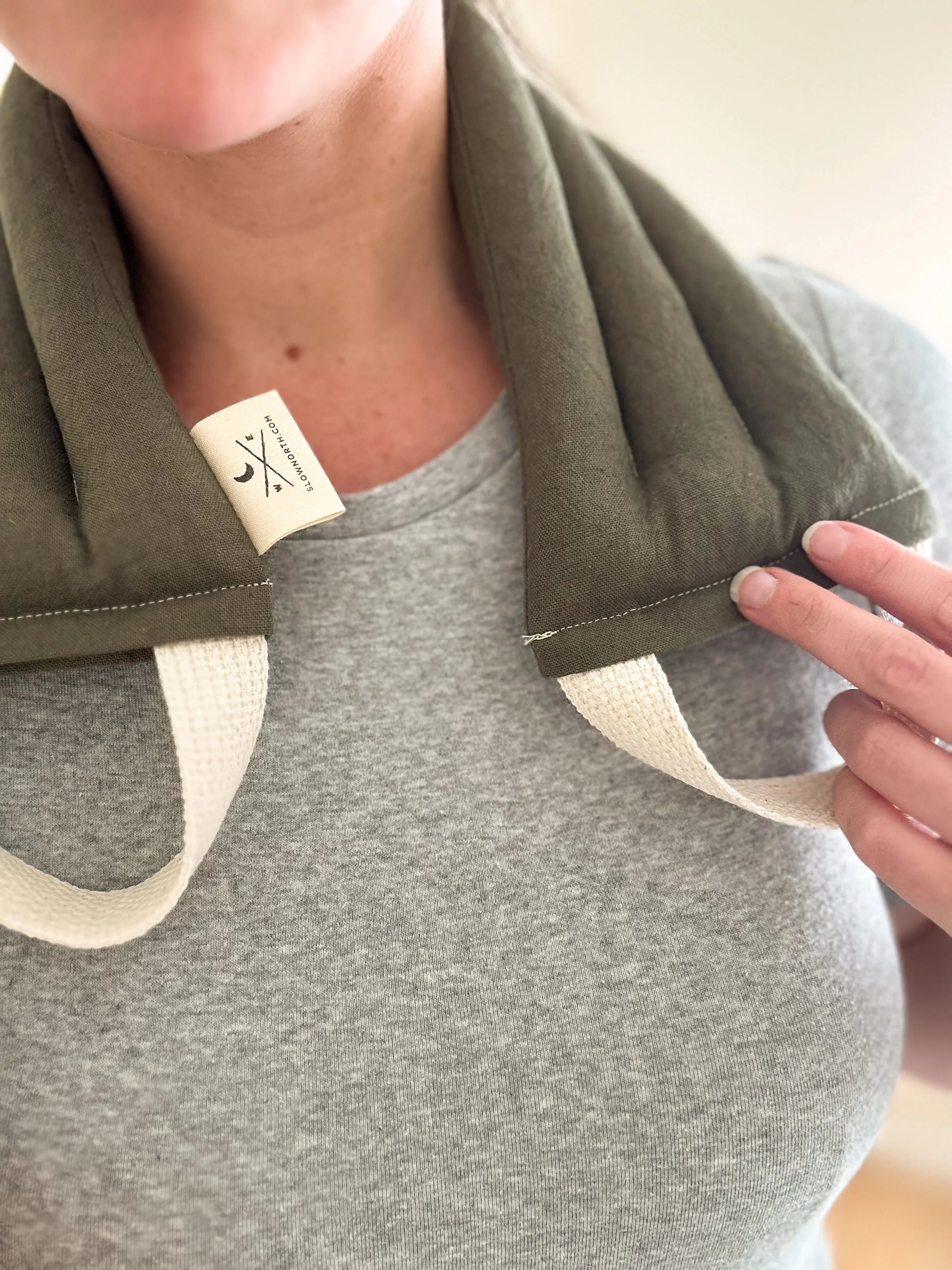 Person wearing olive green neck wrap therapy pack with cream handles on gray shirt
