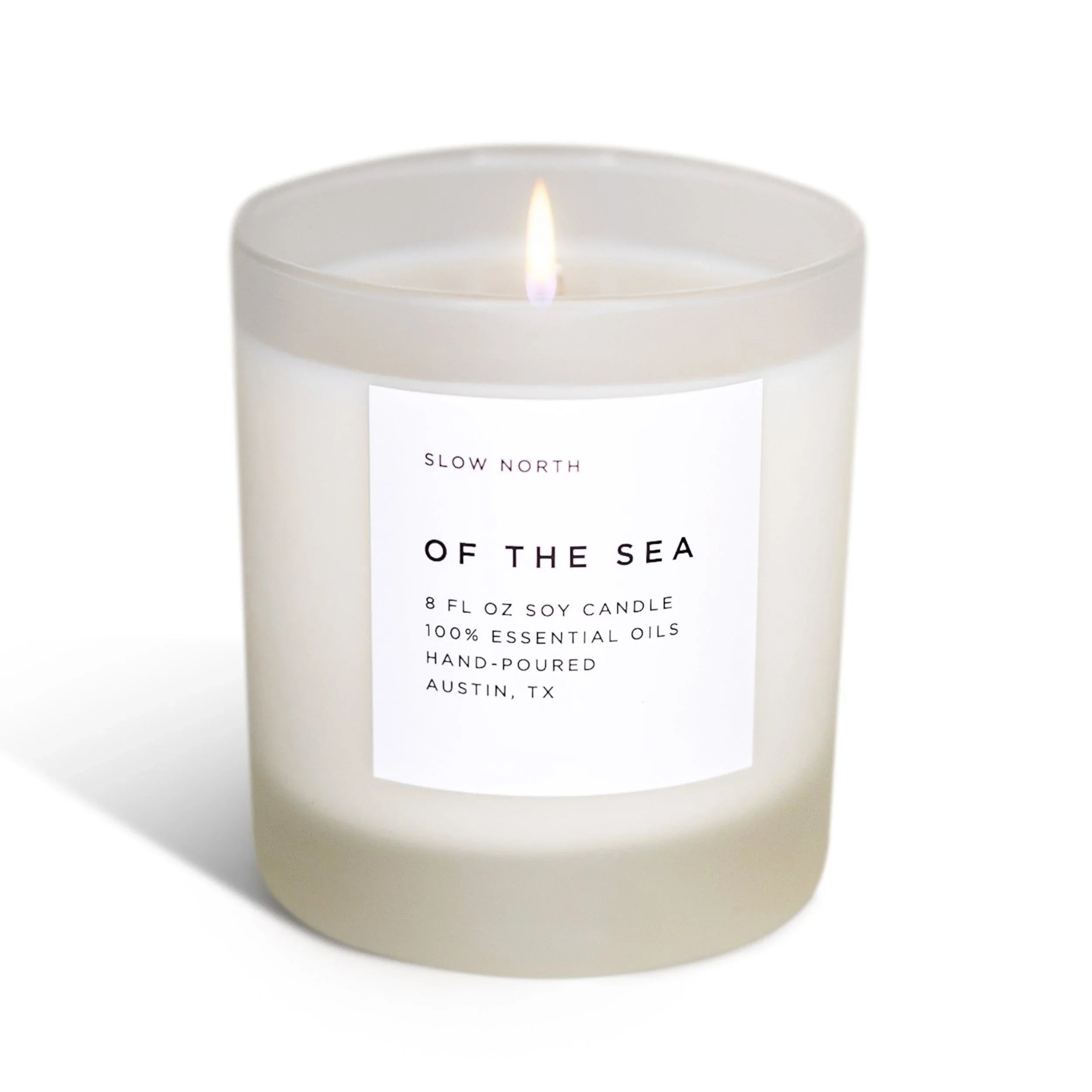Lit 8 oz soy candle in frosted glass with white label reading Of The Sea, hand-poured with essential oils