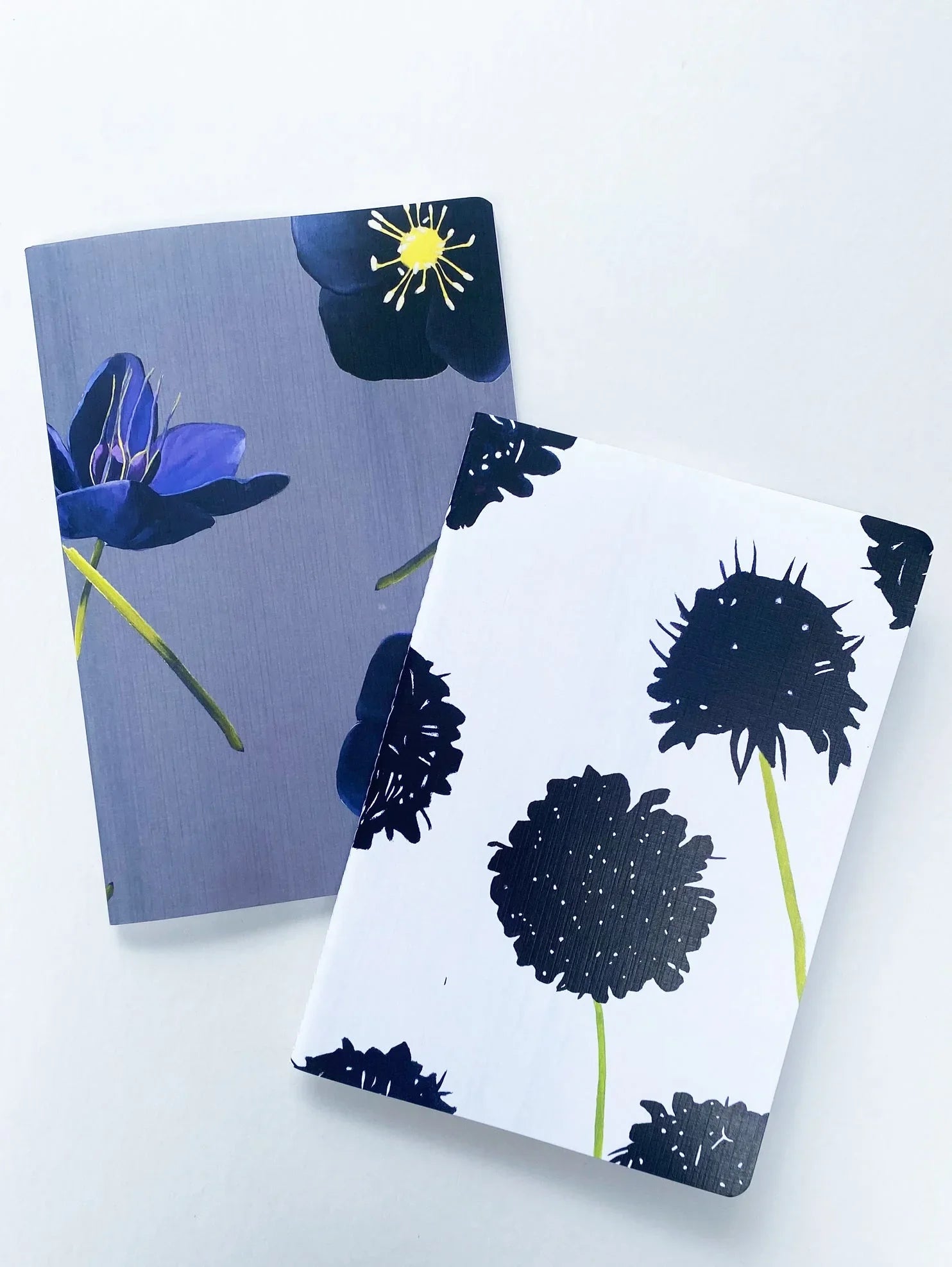 Two floral patterned notebooks on white background, one with black and white flowers, the other with dark blue flowers
