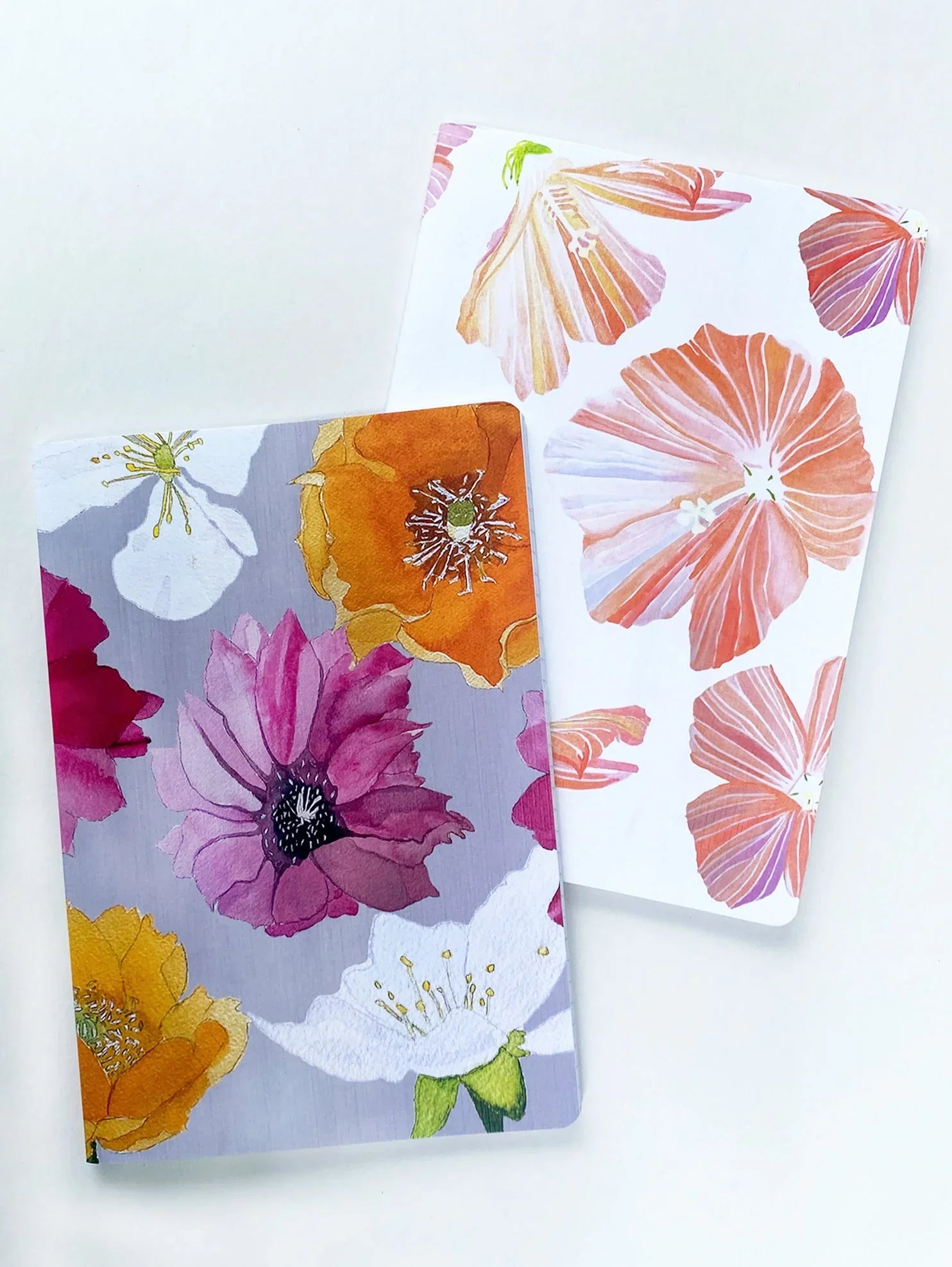 Two notebooks with colorful floral covers featuring hibiscus and cactus flowers on white surface