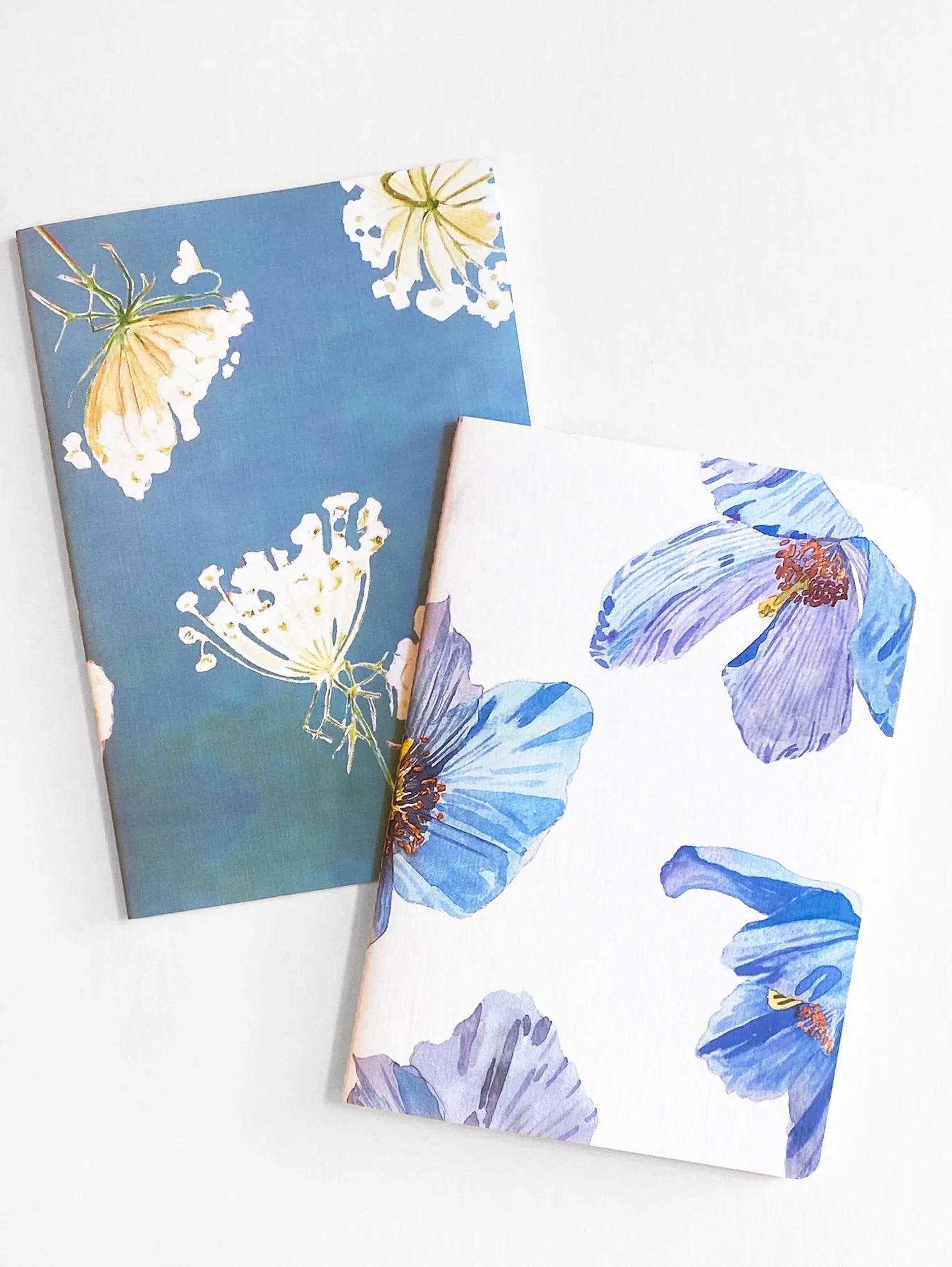 Two floral notebooks, one with white and yellow Queen Anne's Lace on blue, the other with blue Himalayan poppies on white
