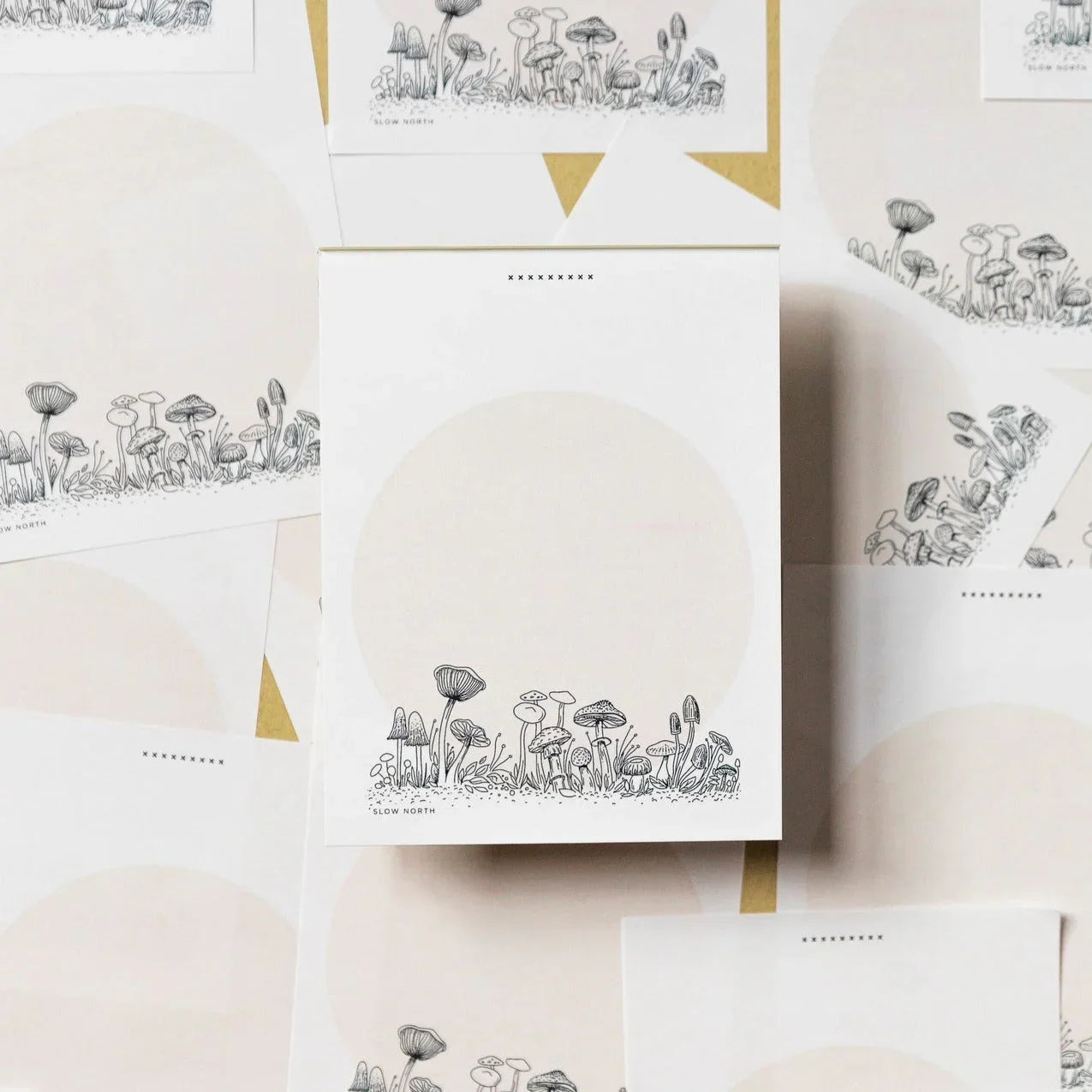 Notepad with black ink mushroom sketches and pale circular background arranged on kraft paper