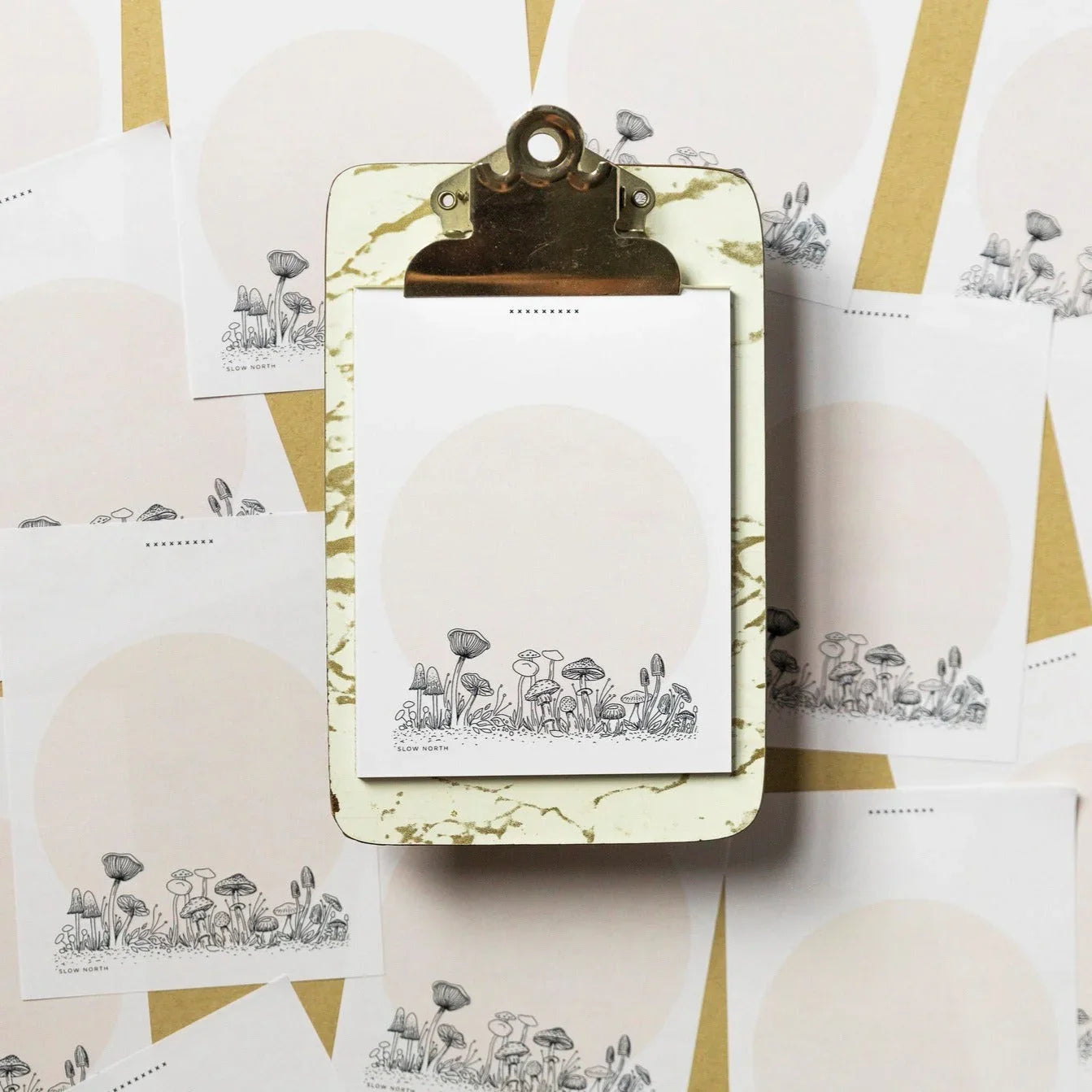Notepad with wild mushroom illustration on marble clipboard, surrounded by matching mushroom design sheets