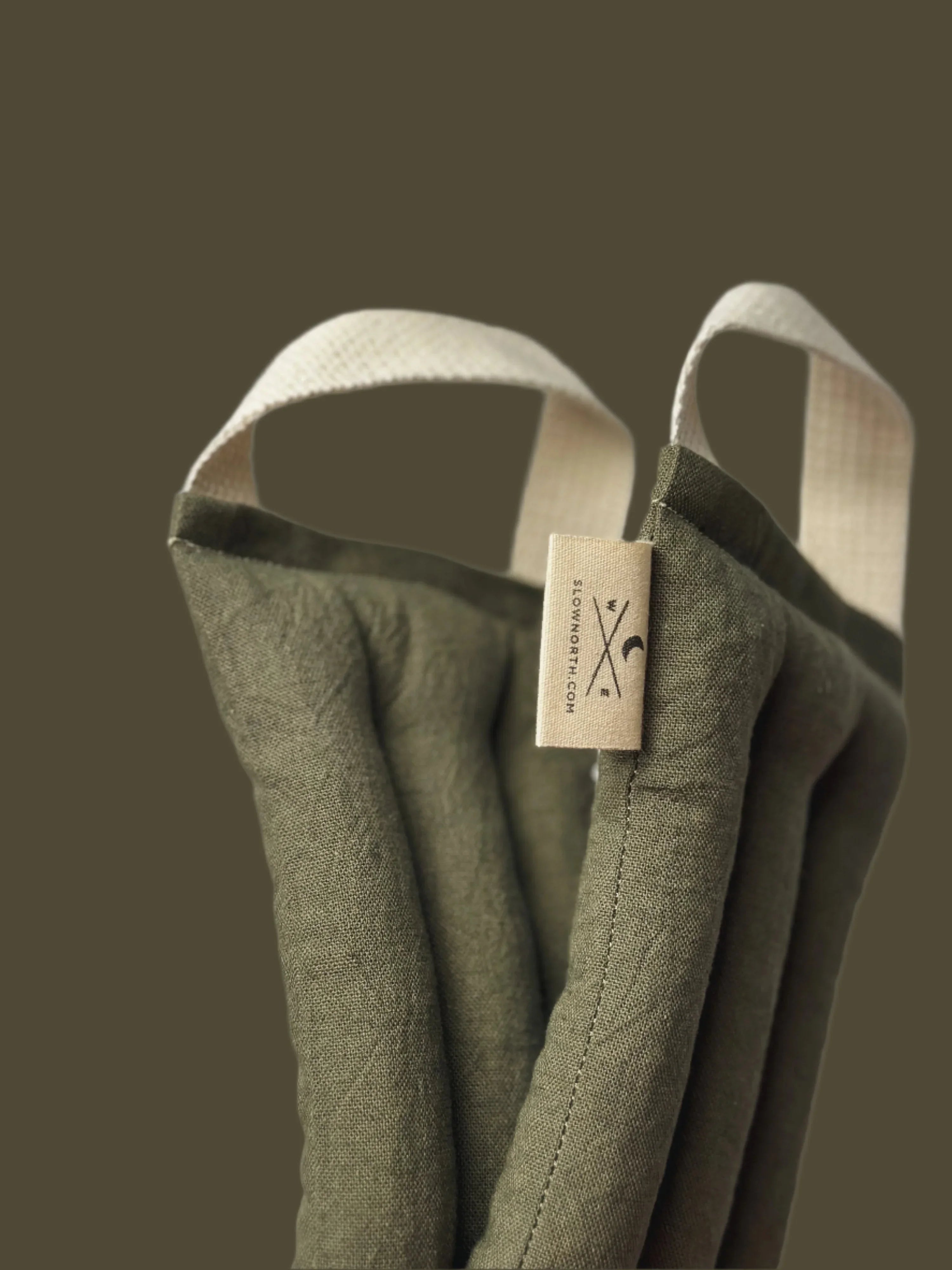 Close-up of olive green neck wrap with stitched fabric and cream hanging loops against dark background